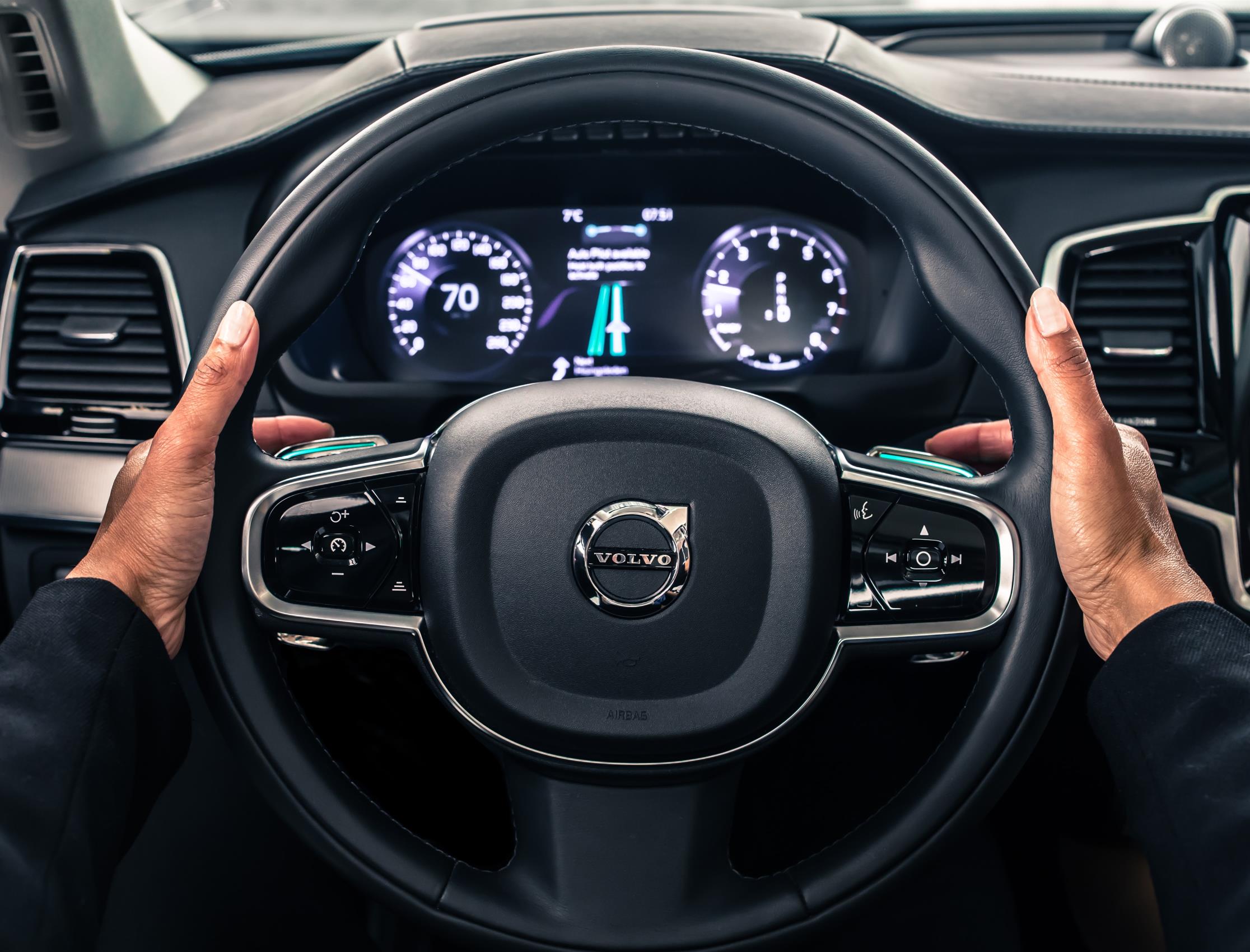 Hands on a Volvo steering wheel showing the dashboard speedometer.