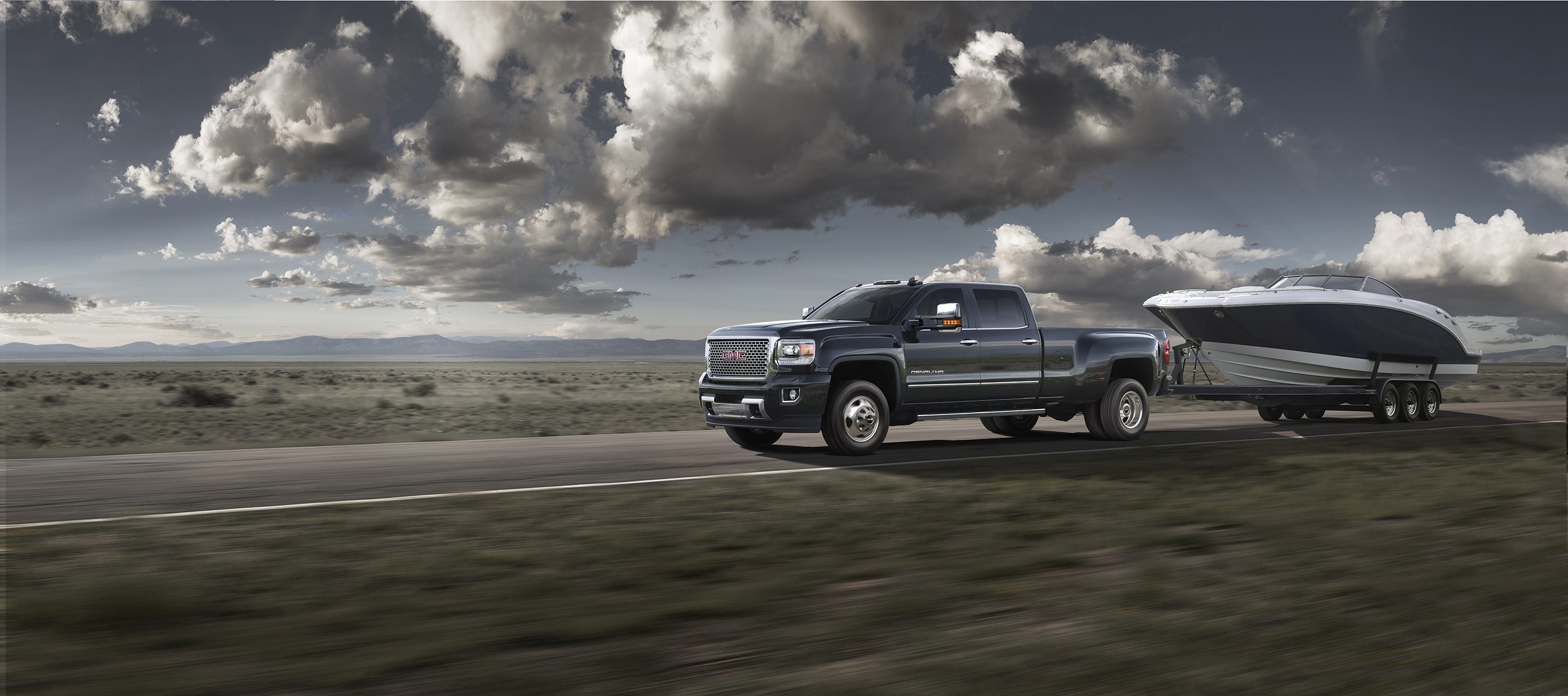 A dark pickup truck driving on an open road under a cloudy sky.