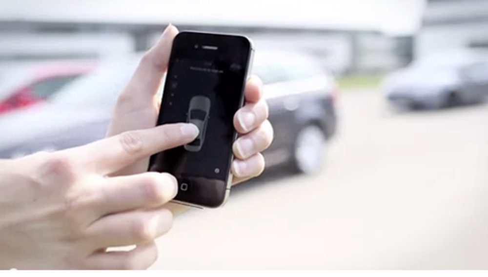 Person unlocking a car using a smartphone app outdoors.