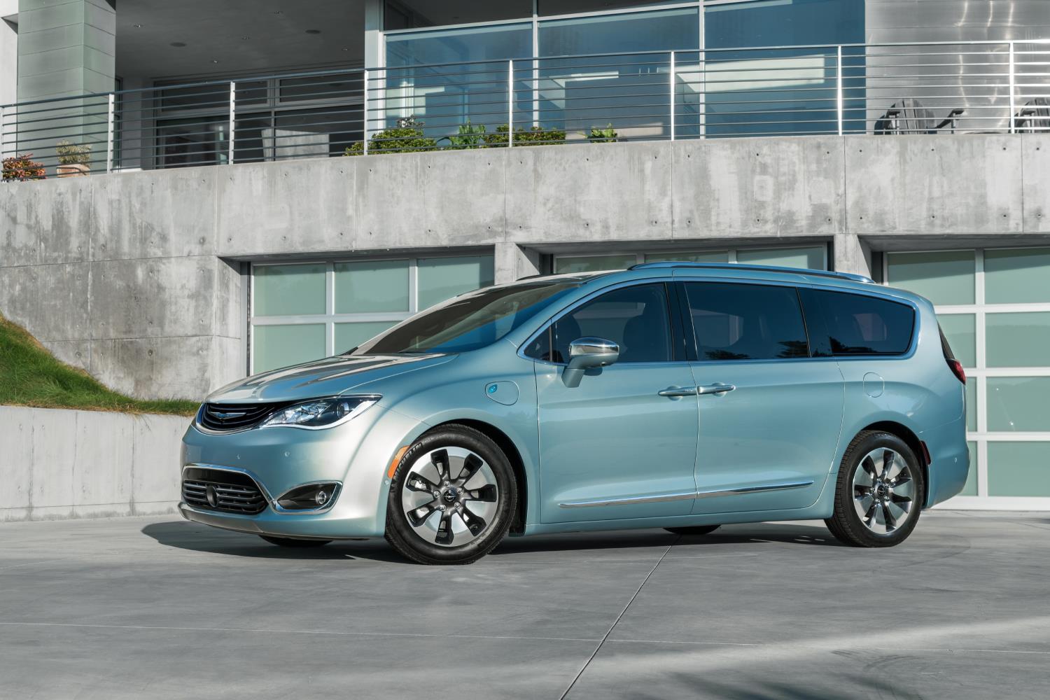 A sleek blue electric minivan parked in front of a modern building.