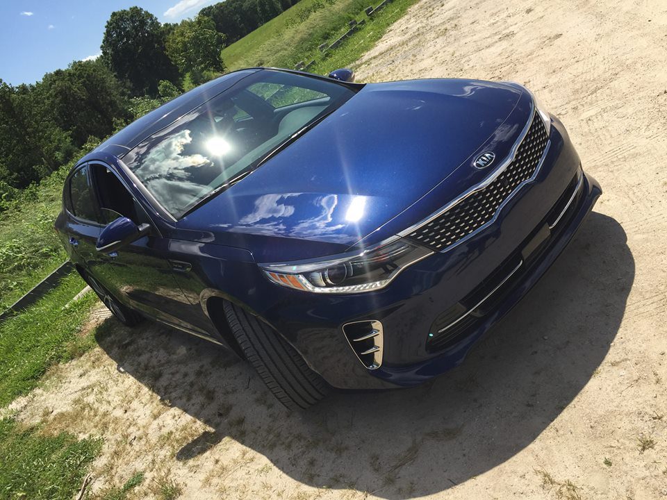 A shiny blue Kia car parked on a dirt road on a sunny day.