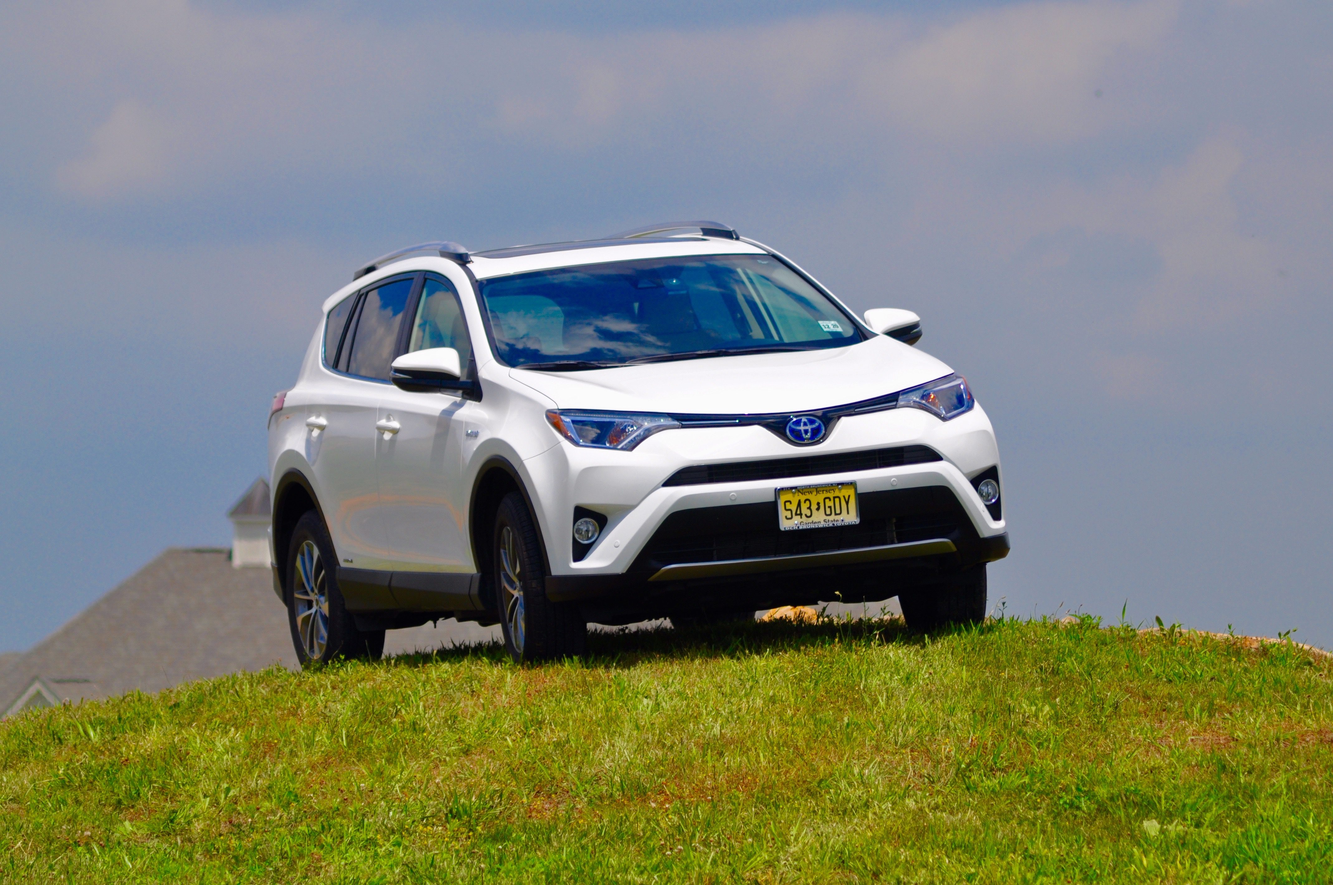 White SUV driving on grassy hill under blue sky.