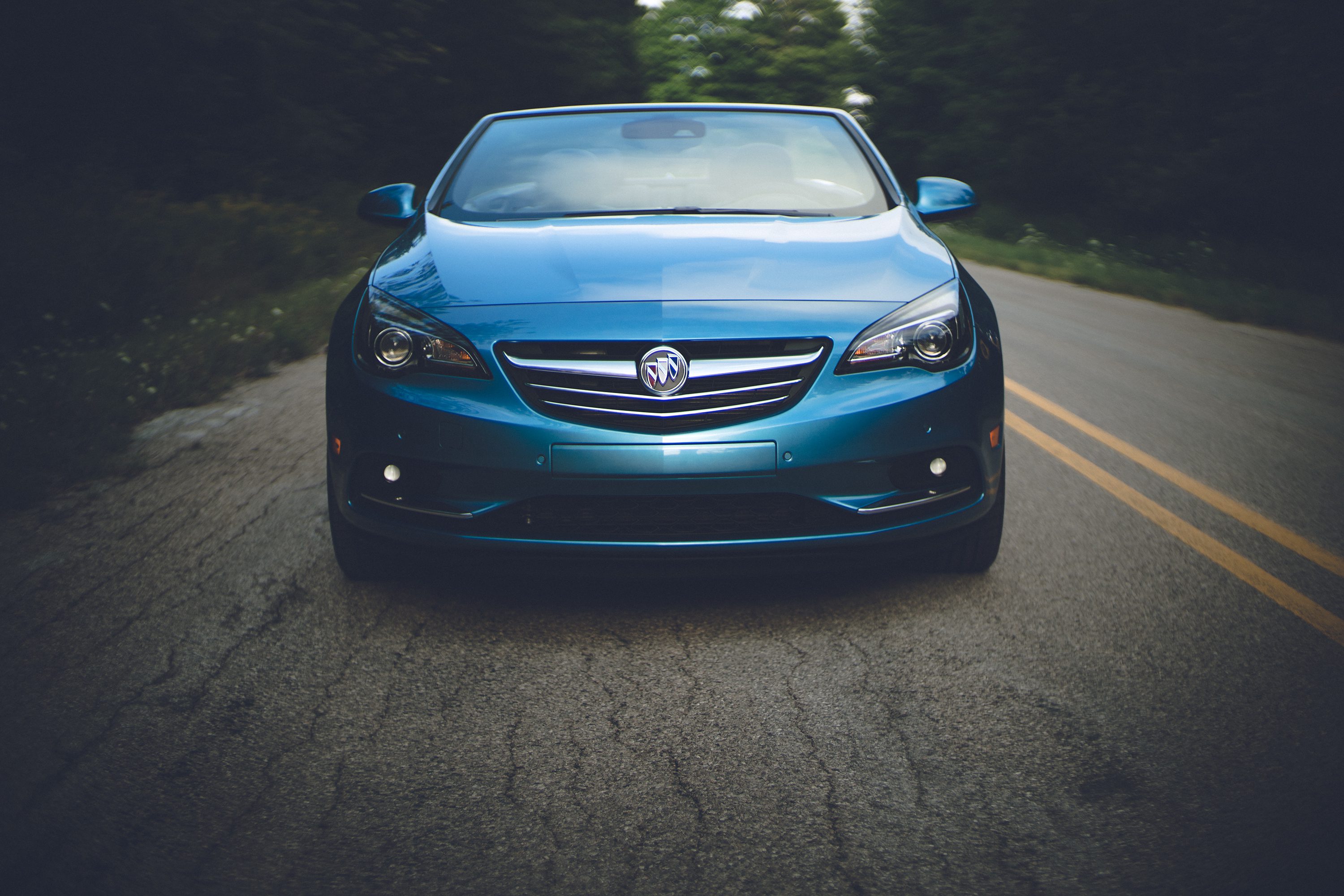 Blue car parked on a road surrounded by greenery.