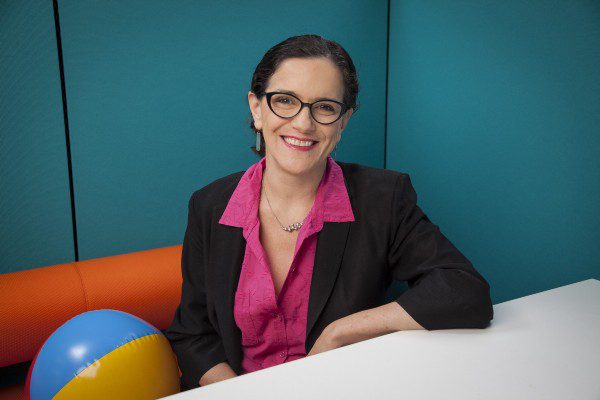 Smiling woman in glasses and business attire at a desk.