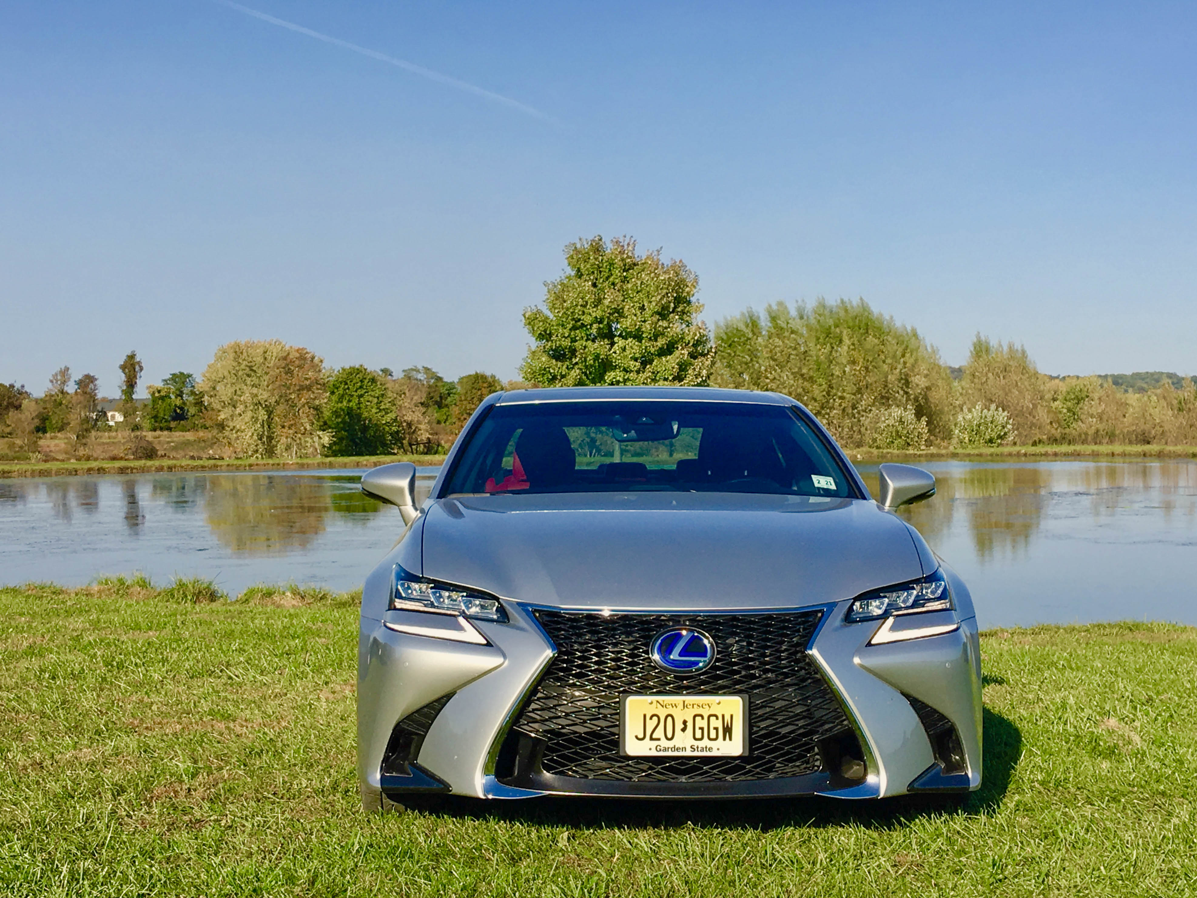 A sleek silver Lexus parked near a serene lake with trees in the background.