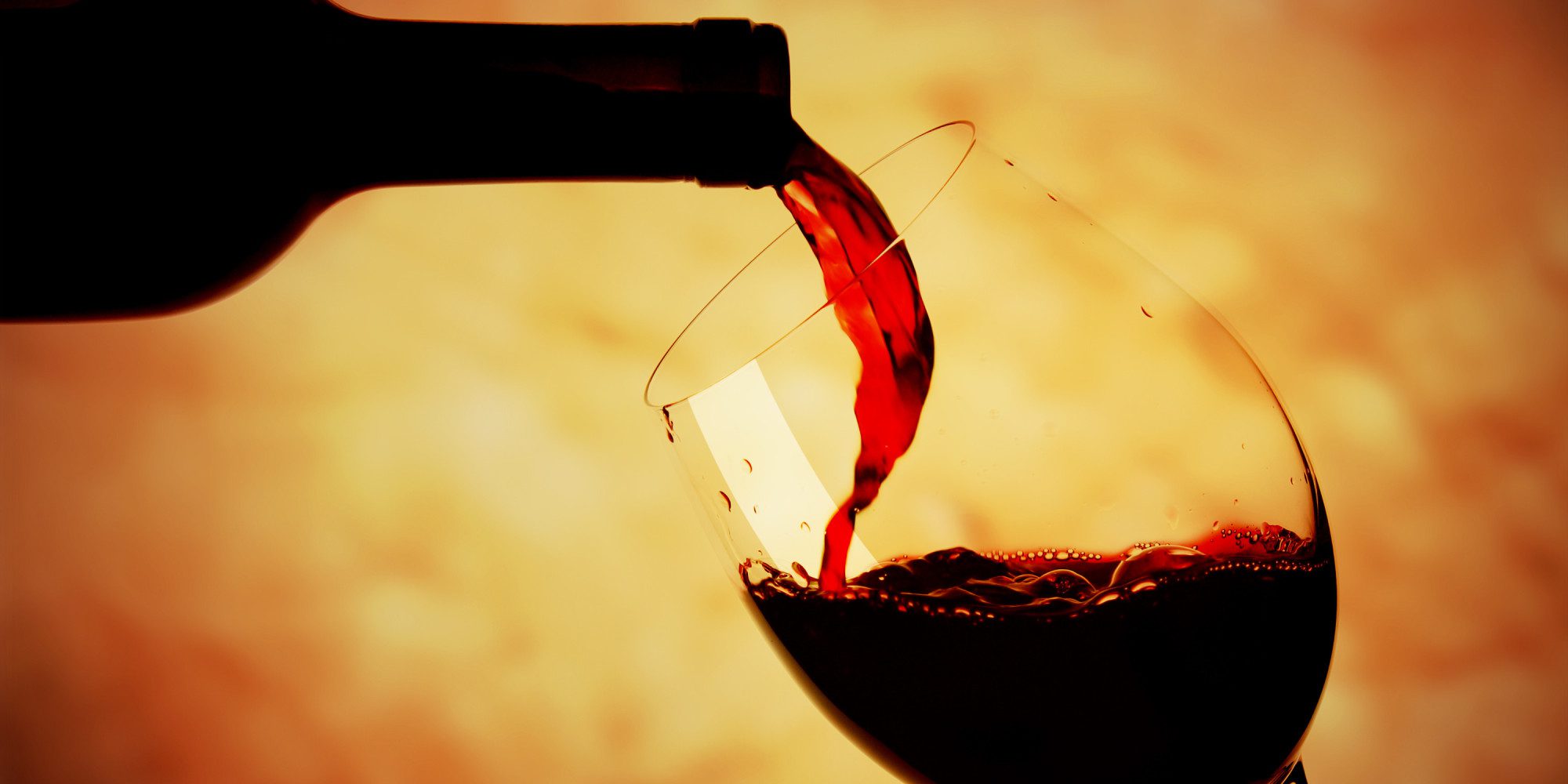 Red wine being poured into a glass against warm light.