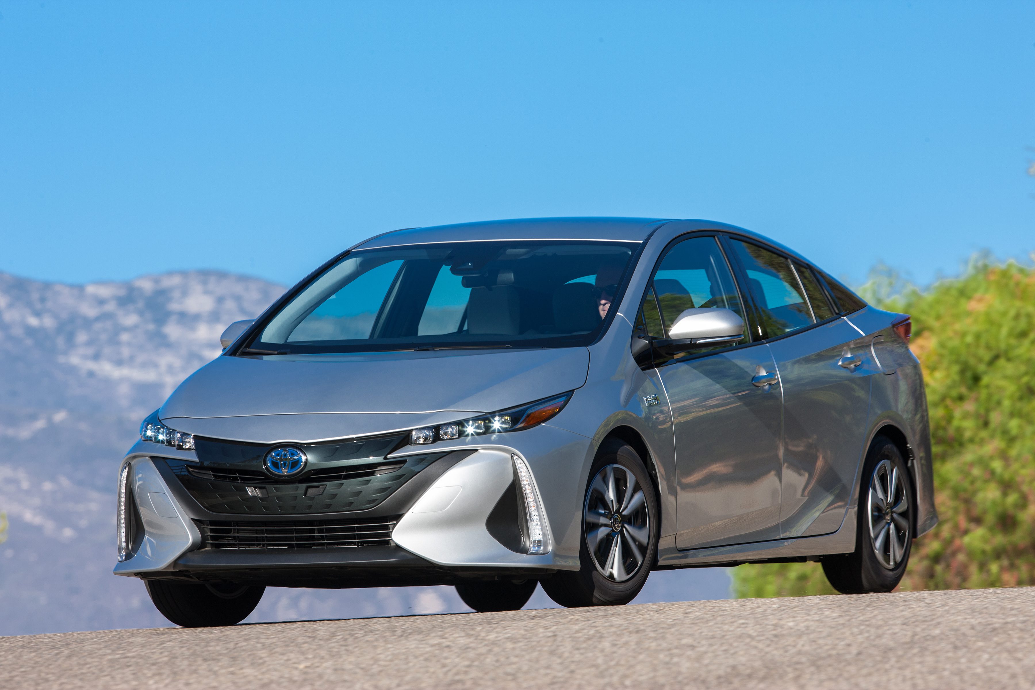 A silver electric sedan parked on an open road under clear blue skies.