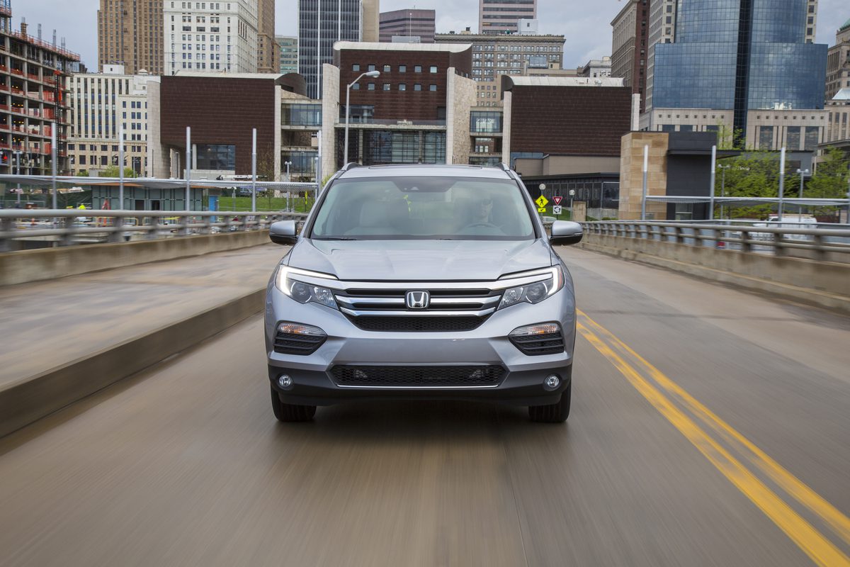 Silver Honda SUV driving on a city bridge with buildings in the background.