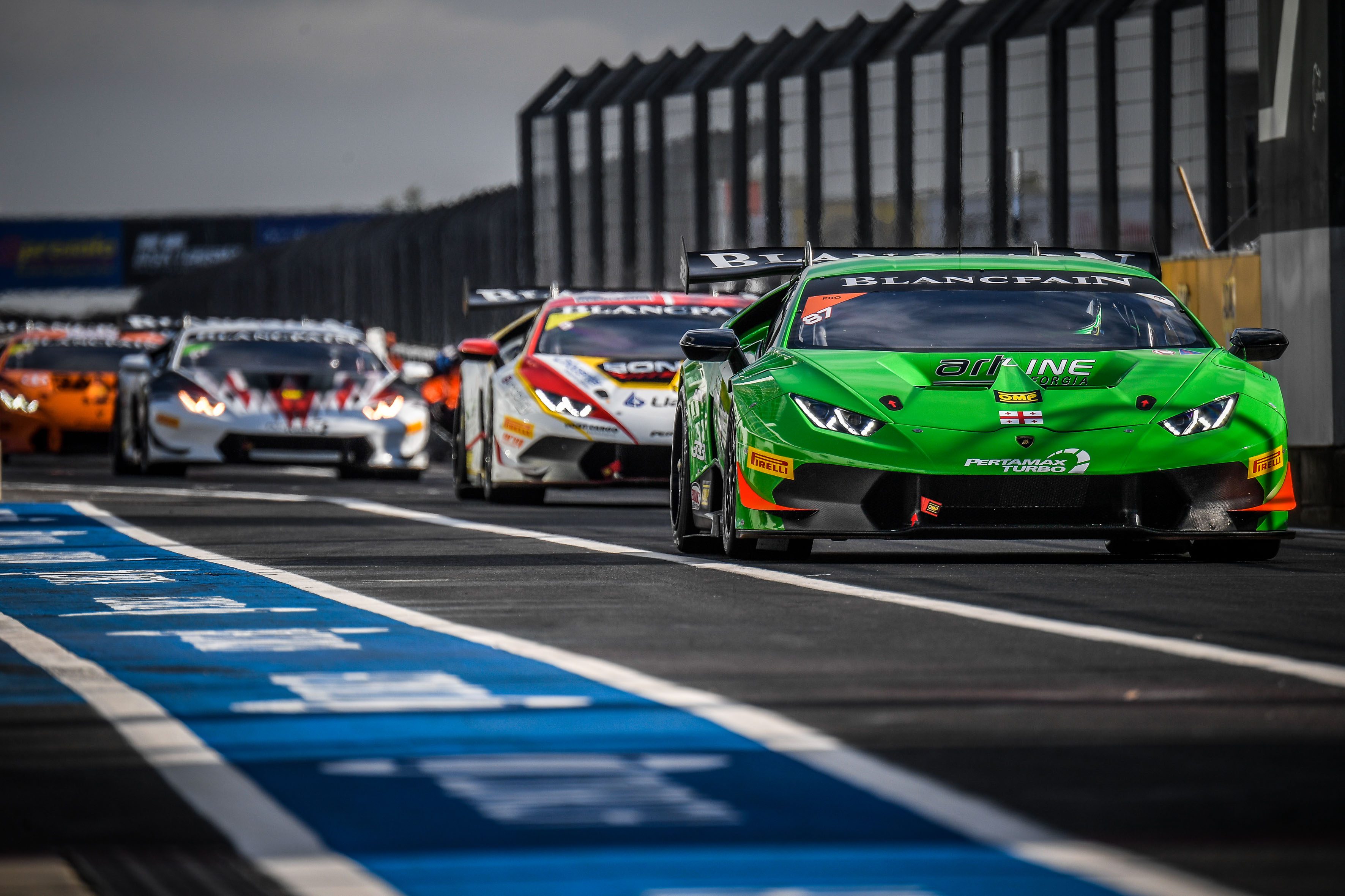 A green race car leads a pack of colorful cars on a racetrack.