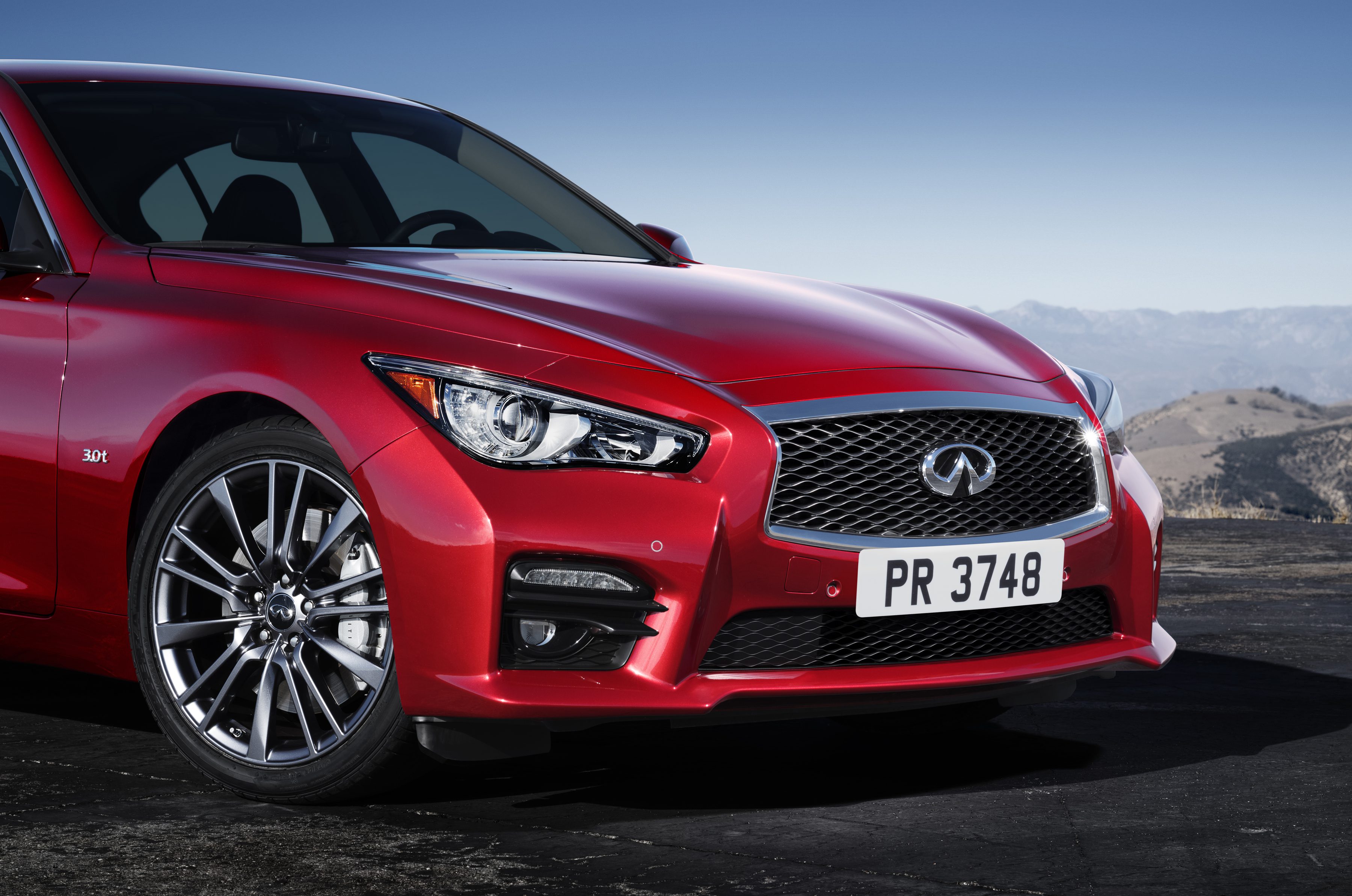 Red Infiniti sports sedan parked with mountains in the background.