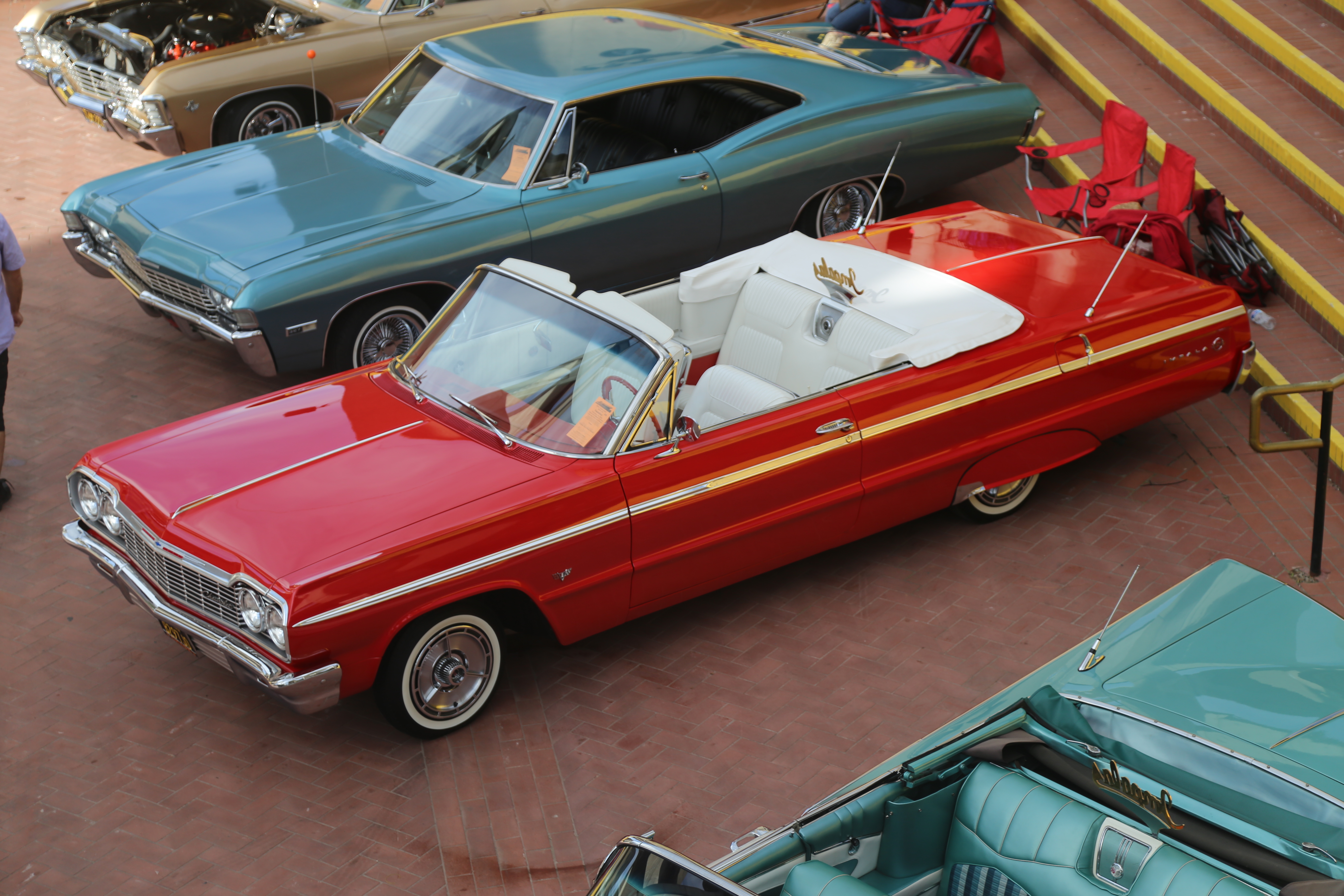 Classic red convertible car parked outdoors with other vintage cars.