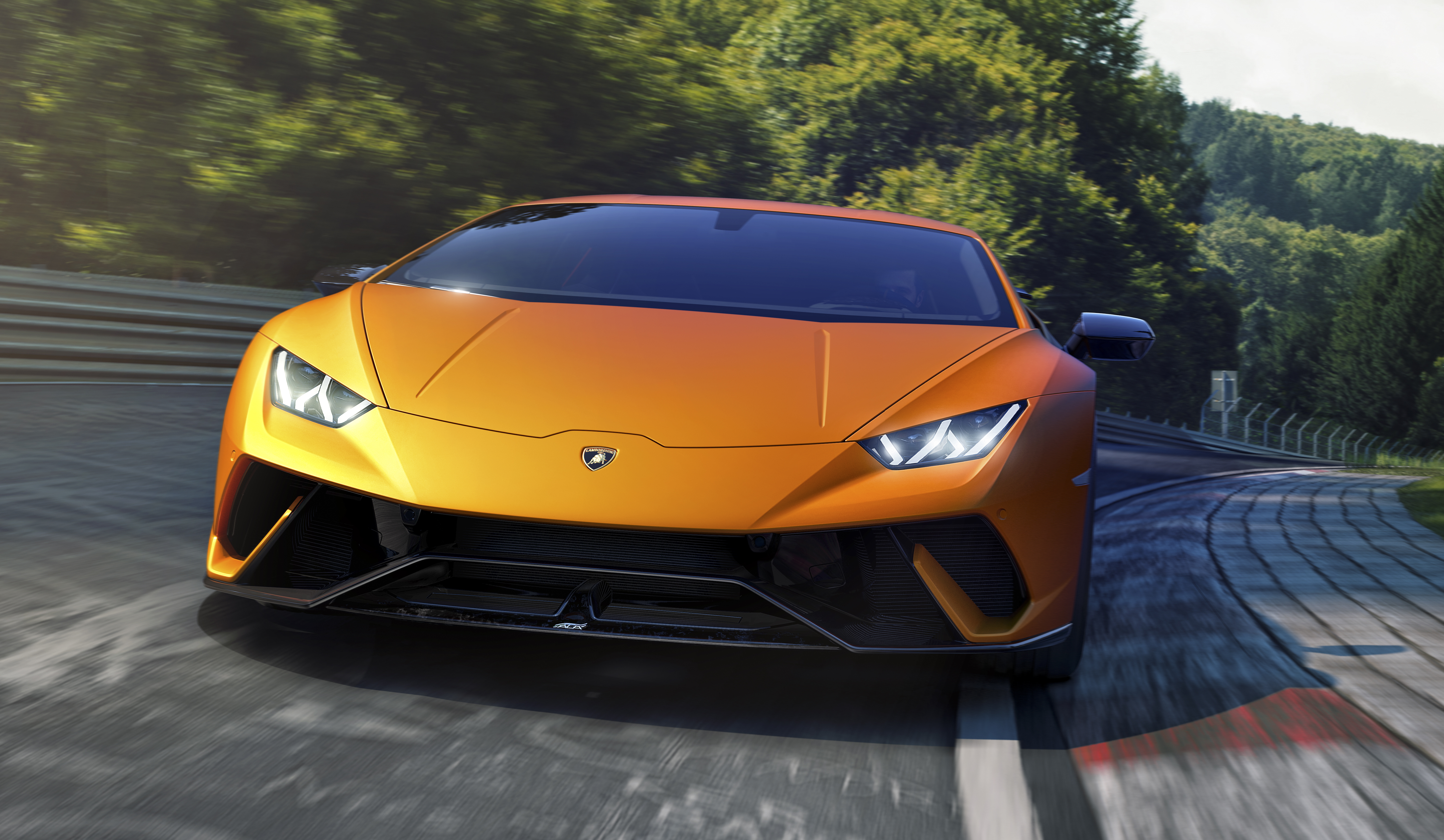 Orange Lamborghini driving on a winding road surrounded by greenery.