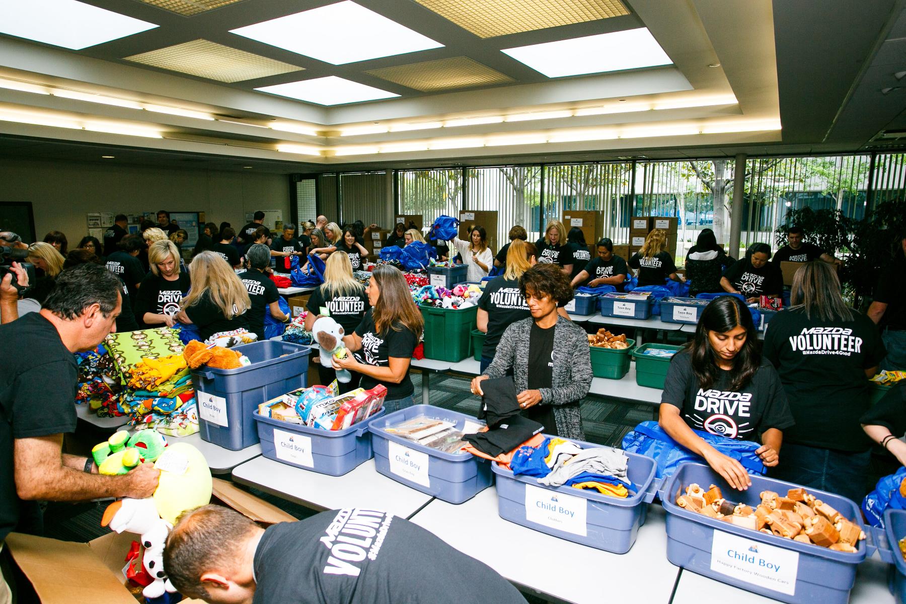 Children and adults sorting items in a bright, busy room with large windows.
