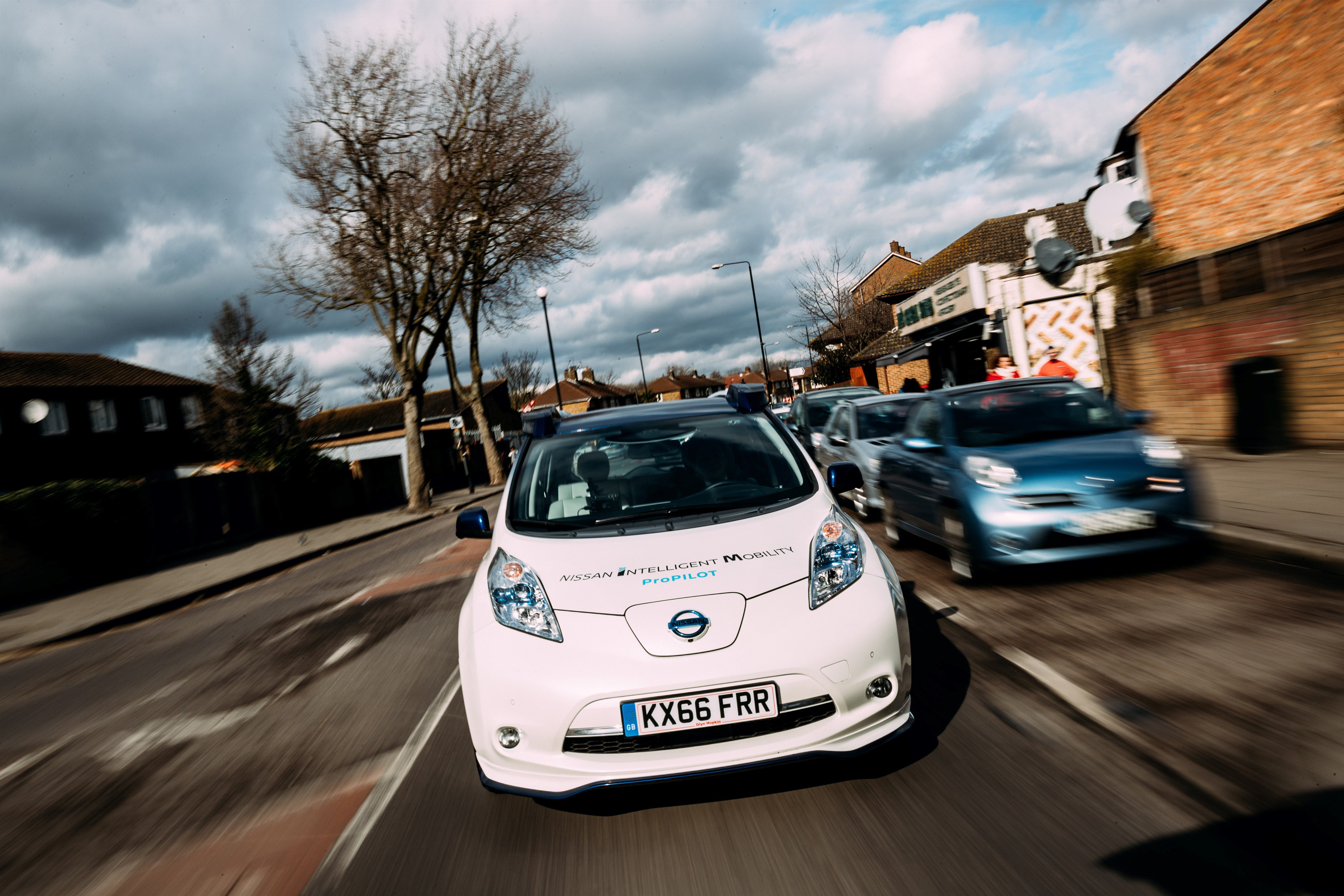 A white electric car driving on a suburban road under a cloudy sky.