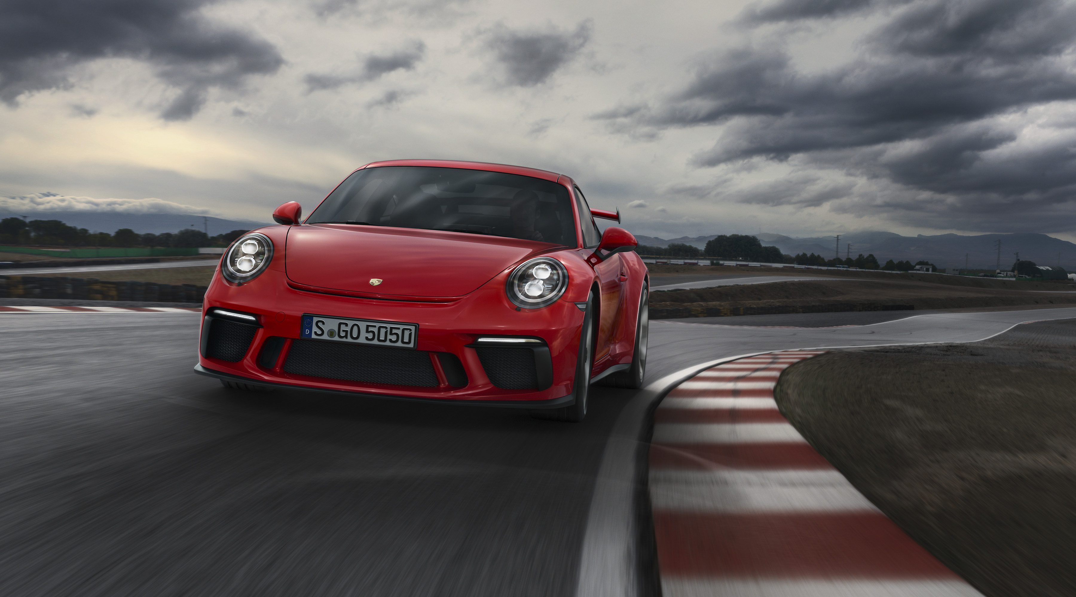 Red sports car taking a sharp turn on a race track under a cloudy sky.