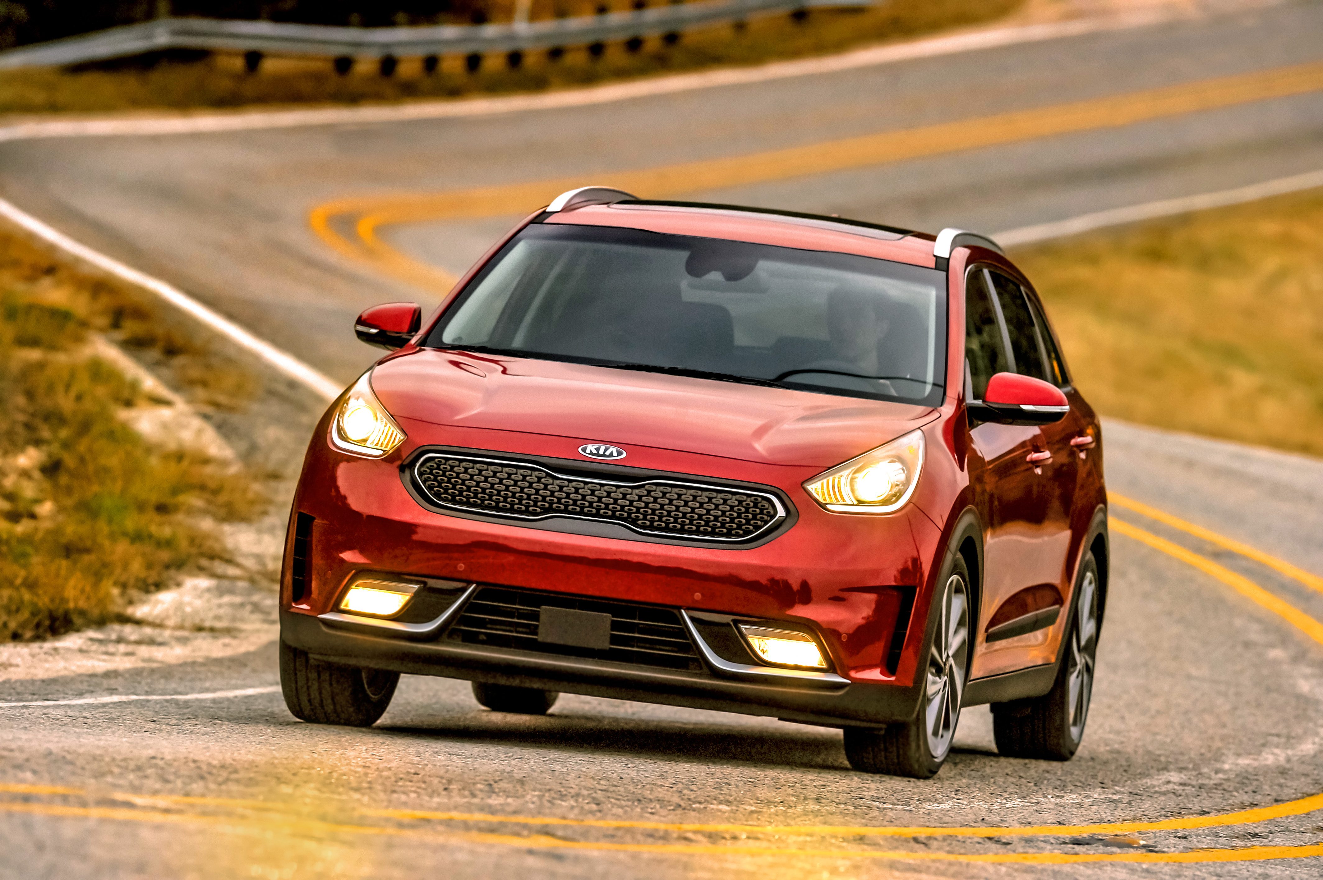 Red car driving on a winding road with headlights on.