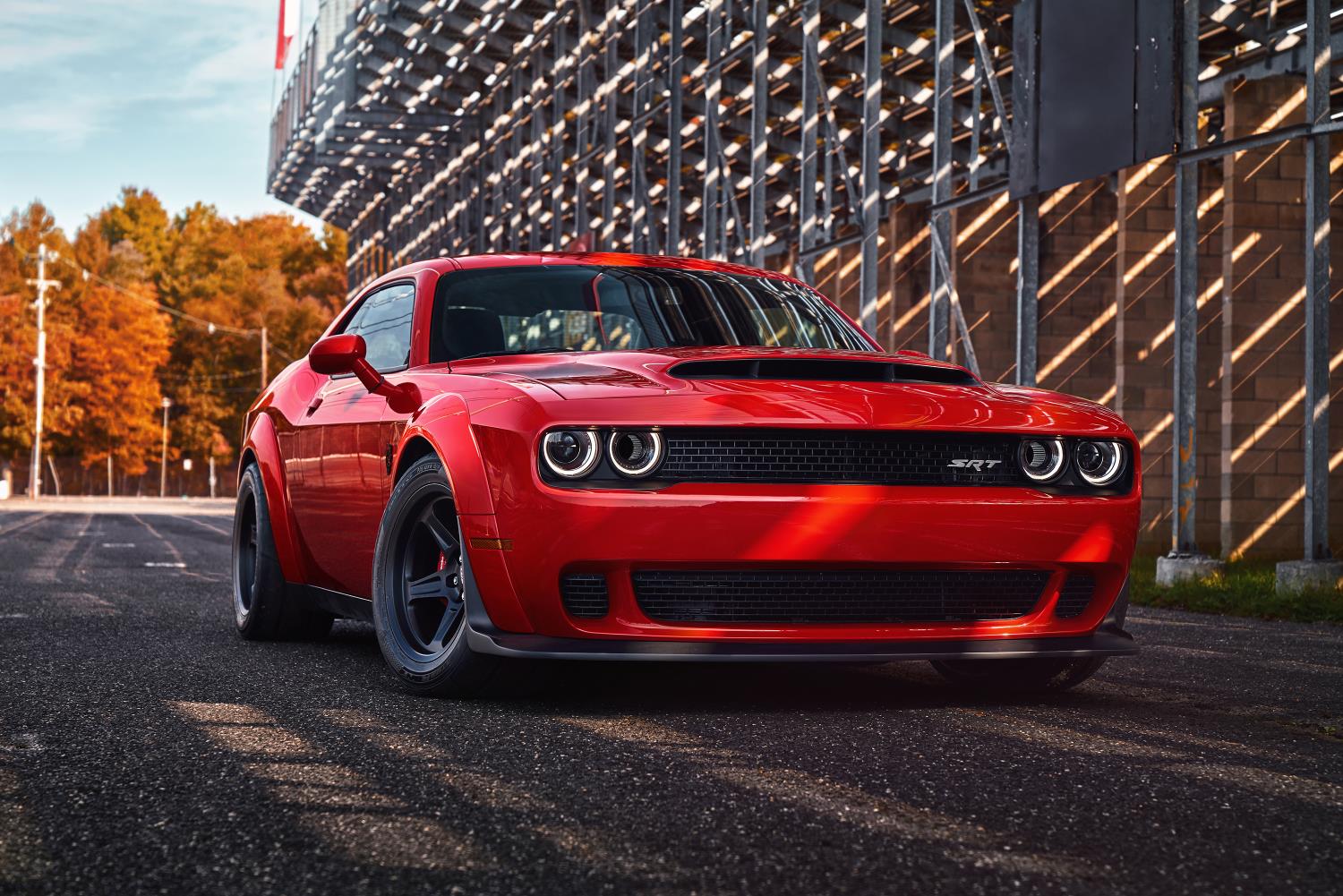 Red muscle car parked near a wooden roller coaster structure.