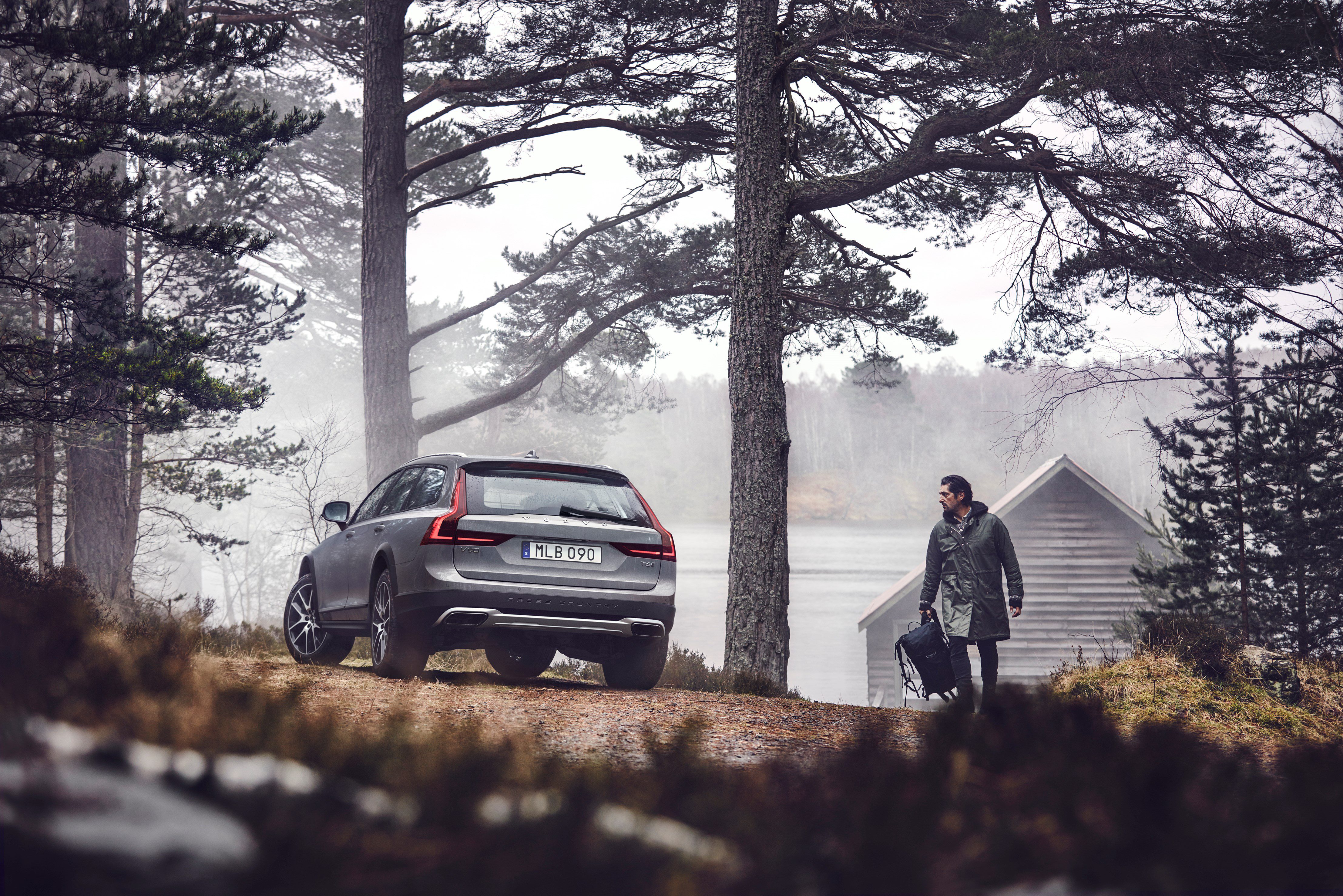A person walking near a parked car in a misty forest.