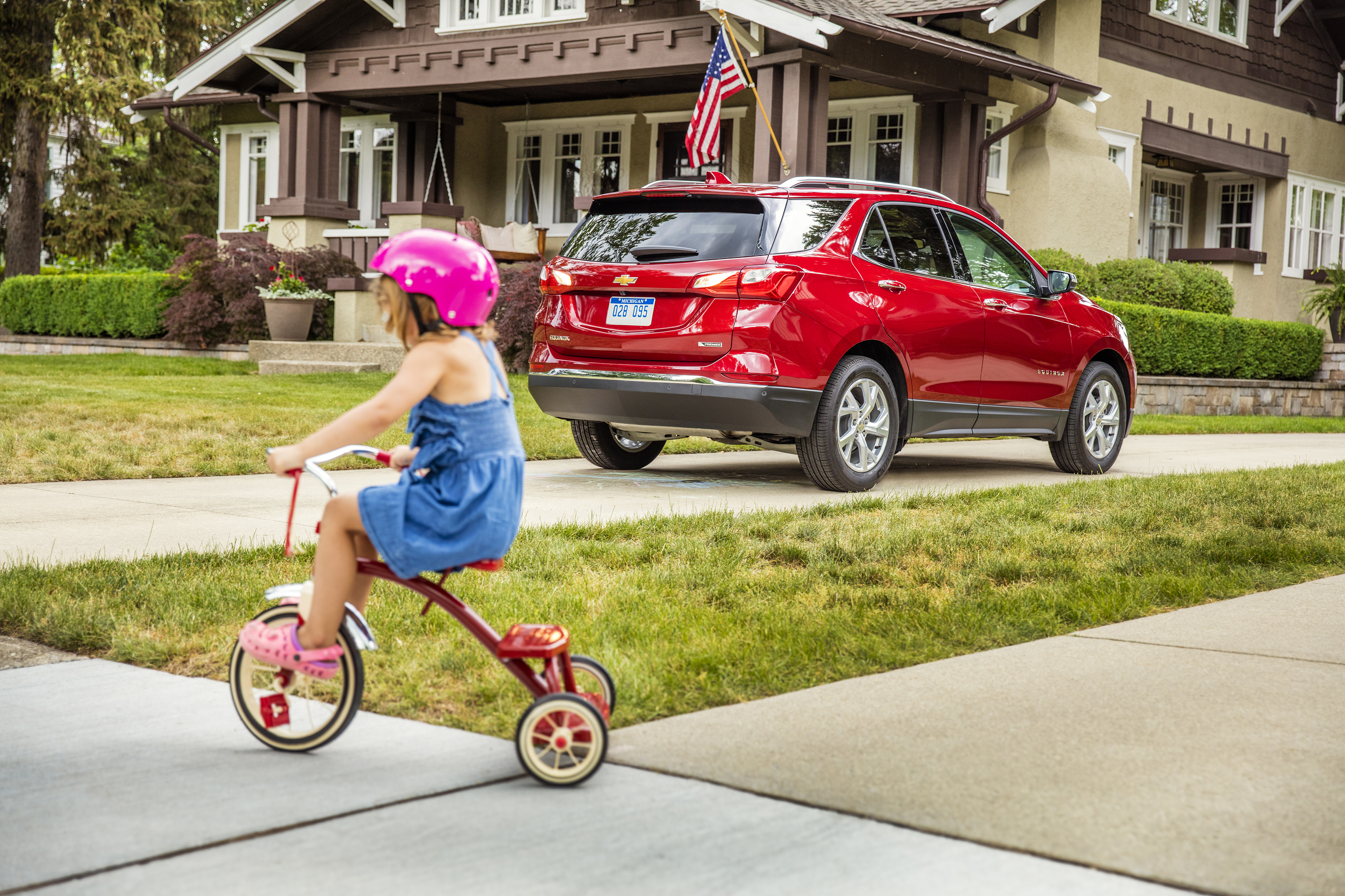 A child rides a tricycle on a sidewalk in a suburban neighborhood.