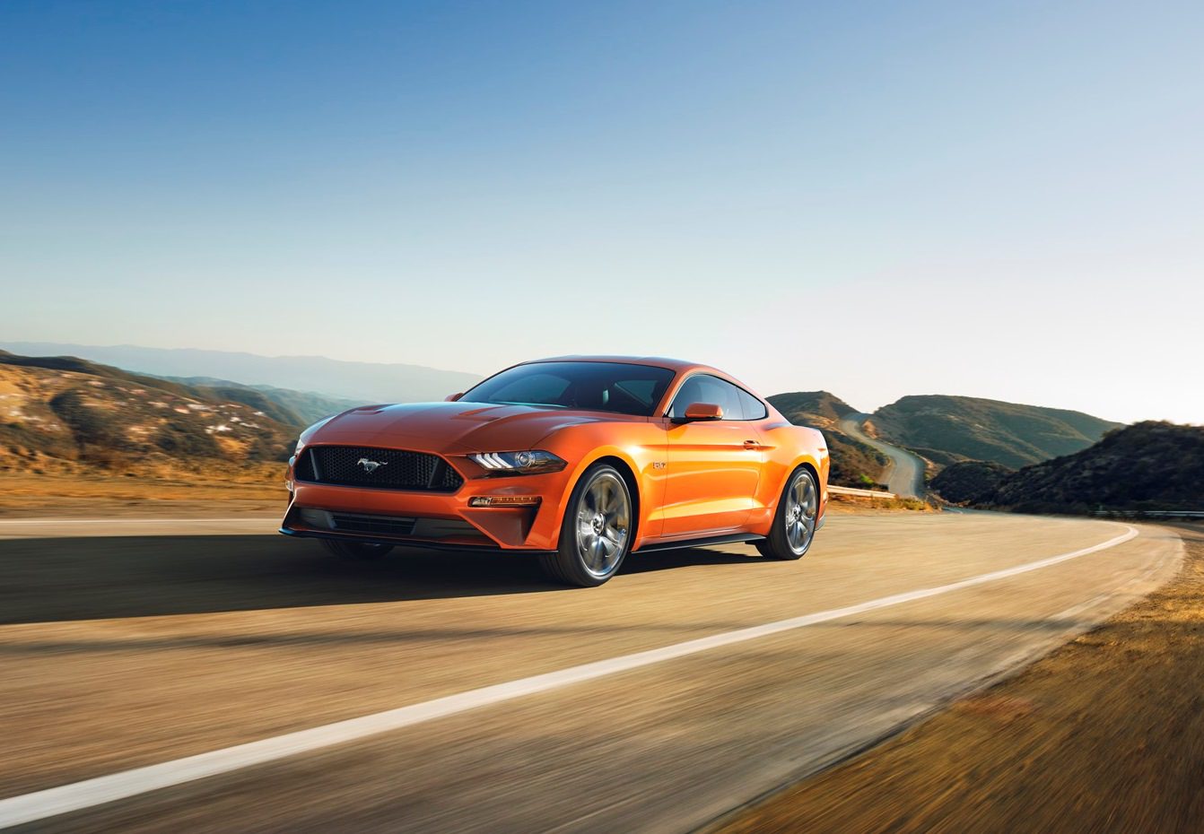 Orange sports car driving on an open highway during daytime.