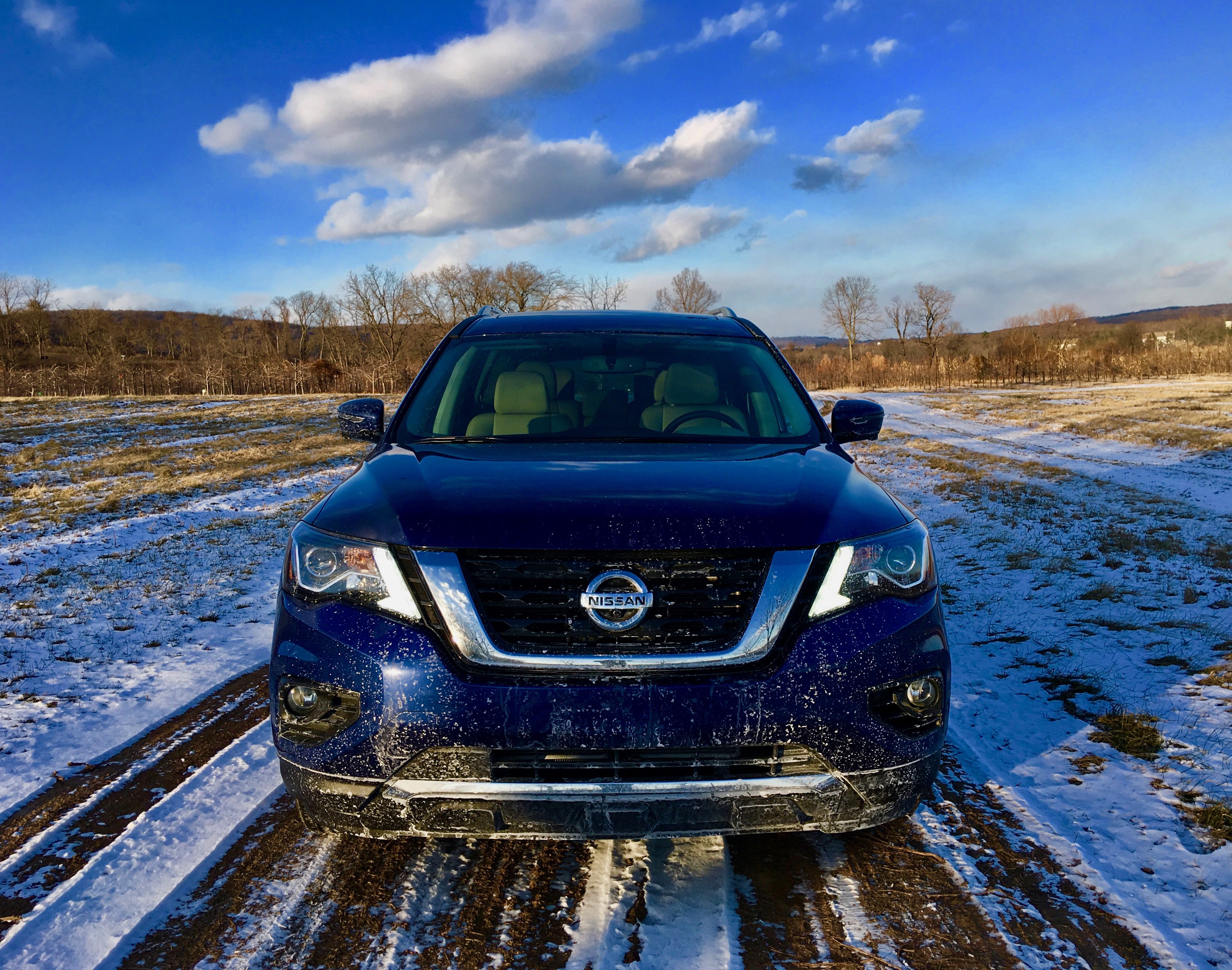 Blue Nissan SUV parked on a snowy rural road under a bright sky.