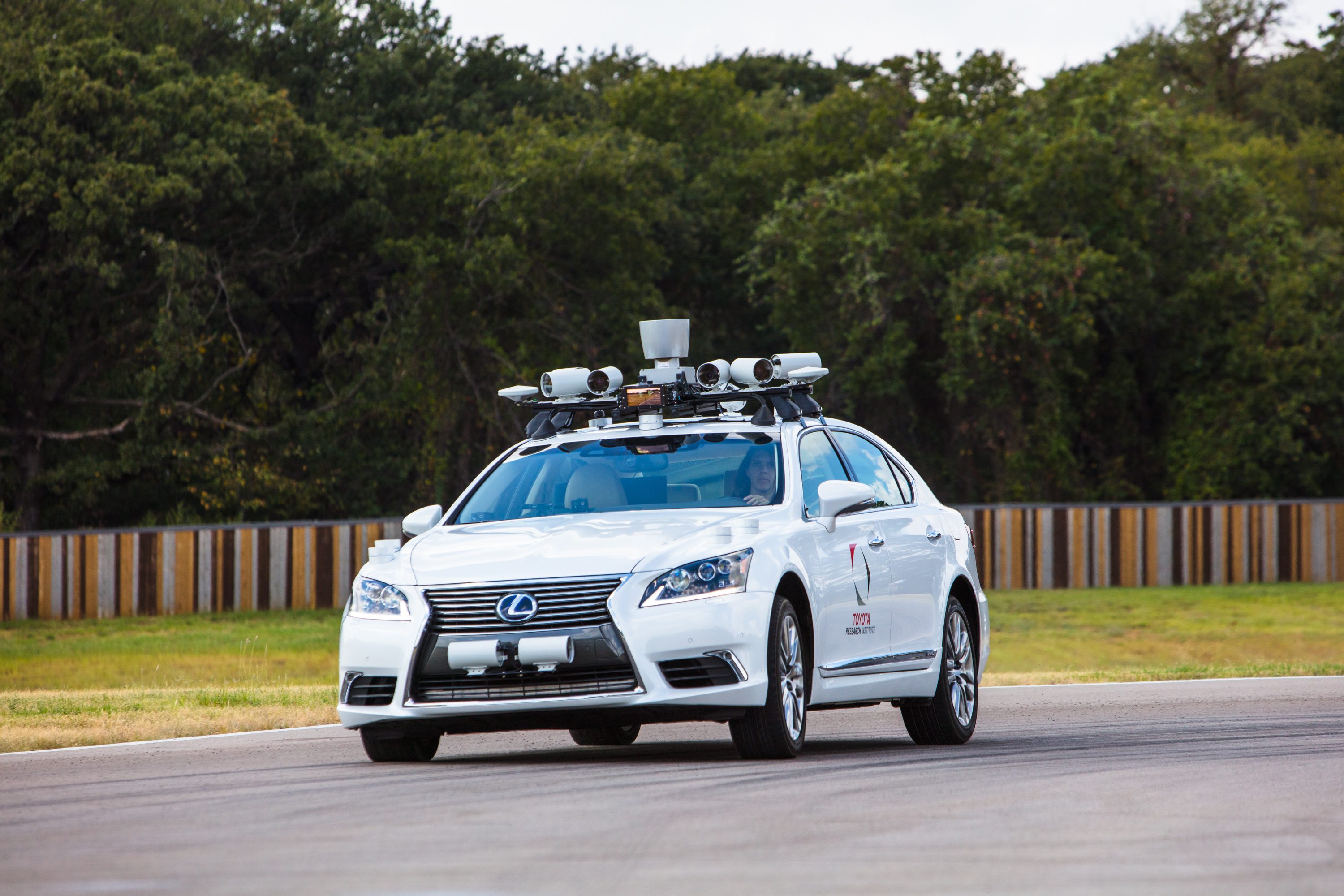 White autonomous Lexus car equipped with sensors driving on a test track.