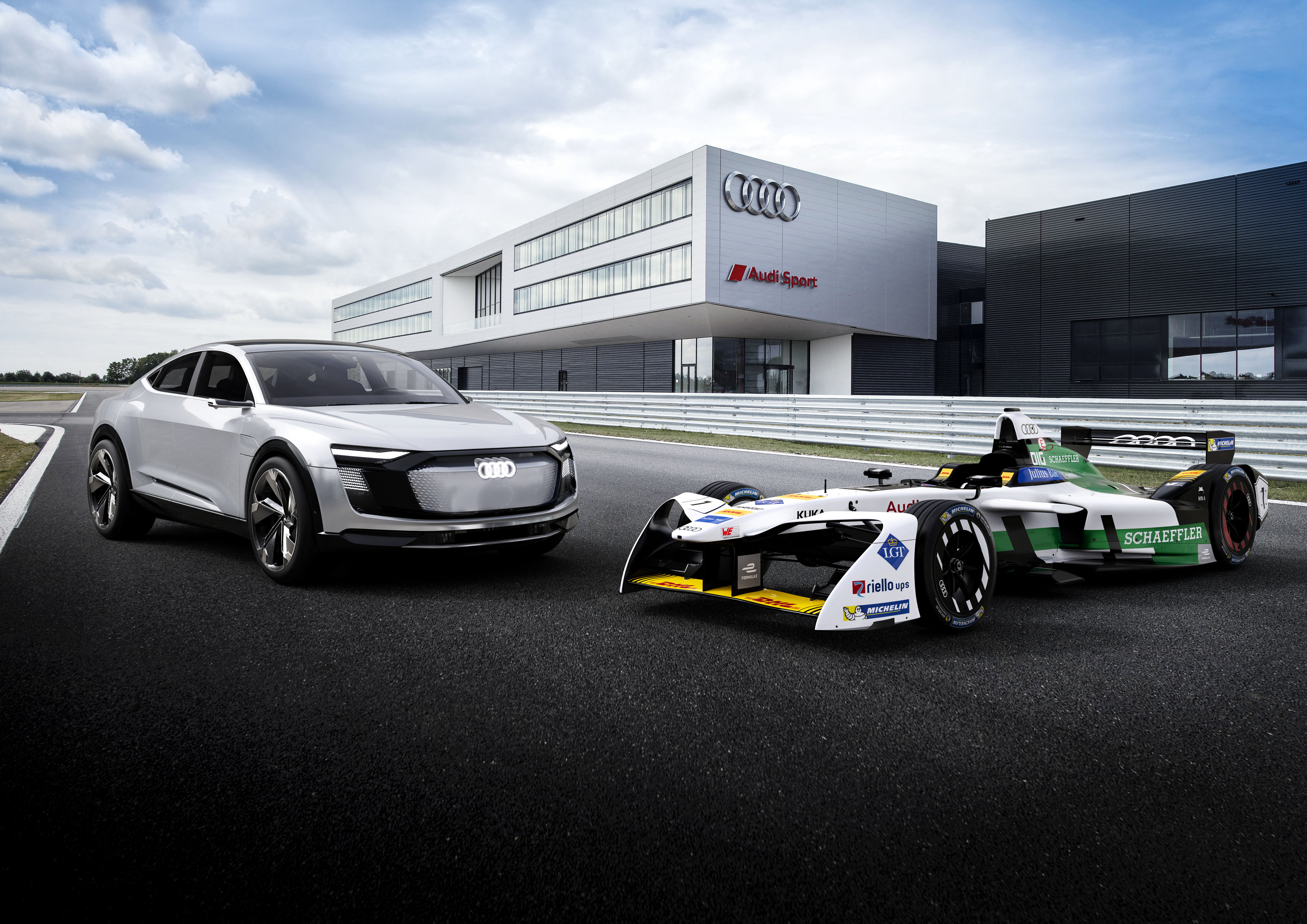 Audi electric and race cars parked outside a modern Audi building.
