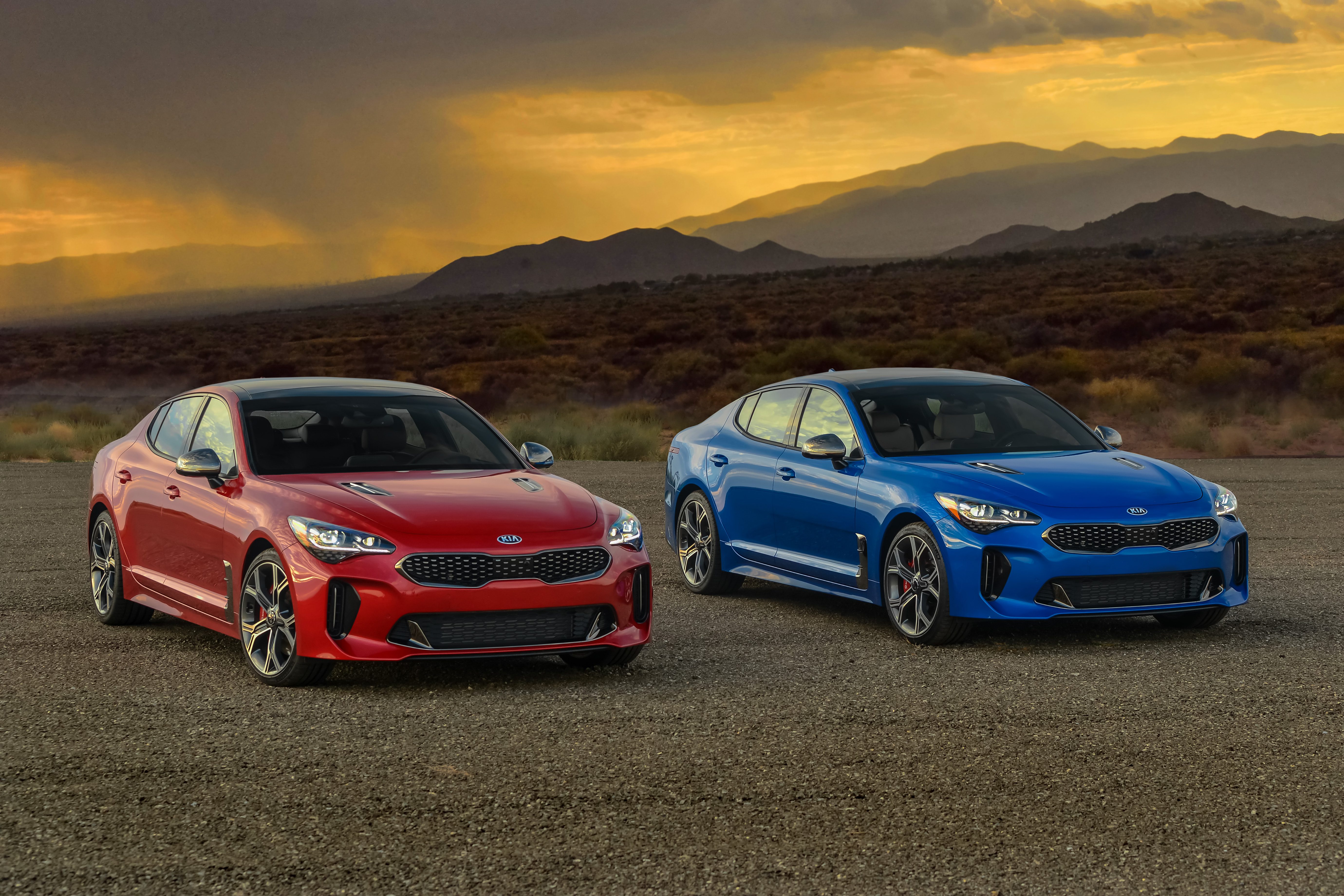 Two sporty cars, one red and one blue, parked on a desert road at sunset.