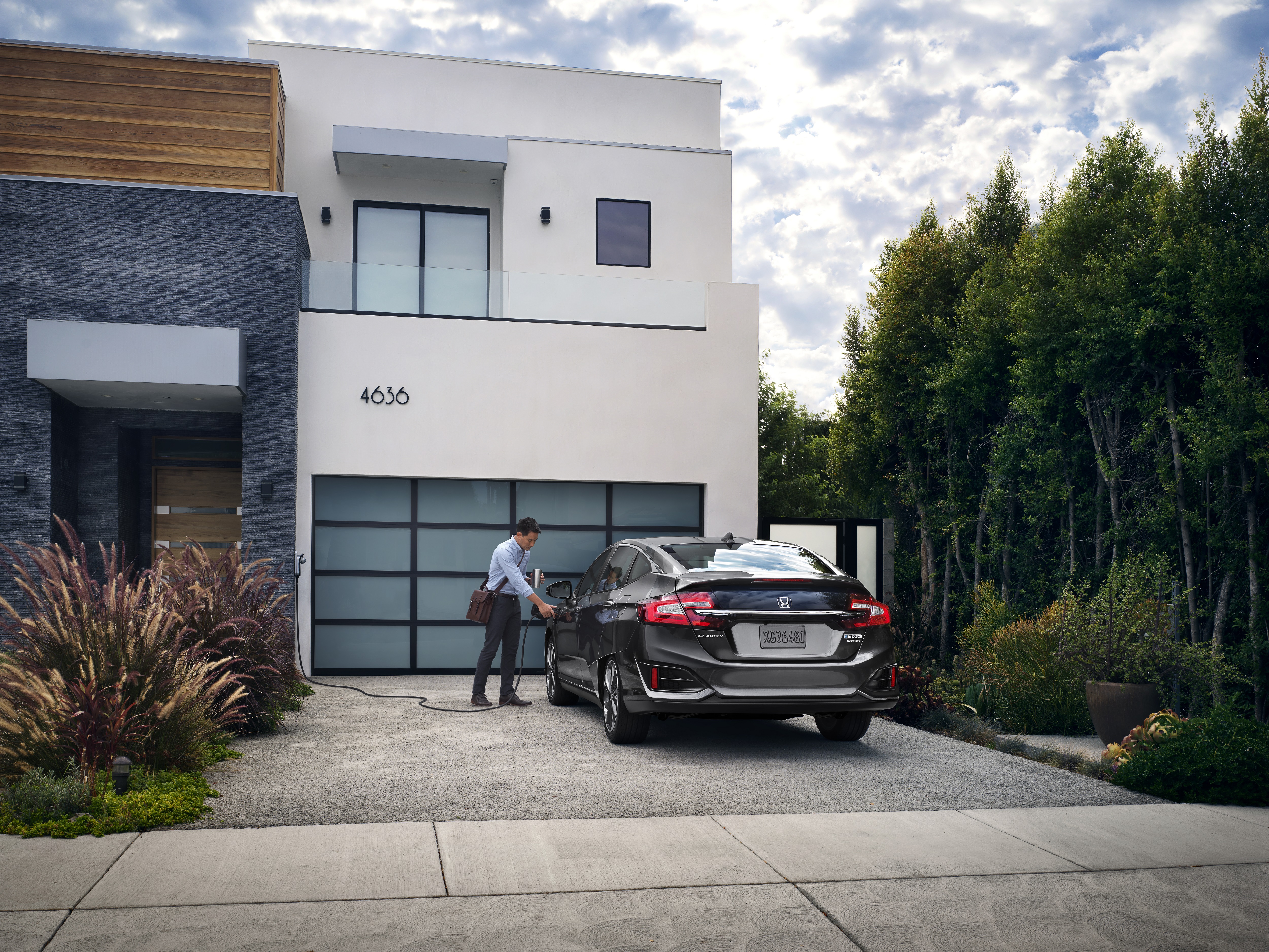 Modern house with a car parked in front and a man standing by the driveway.