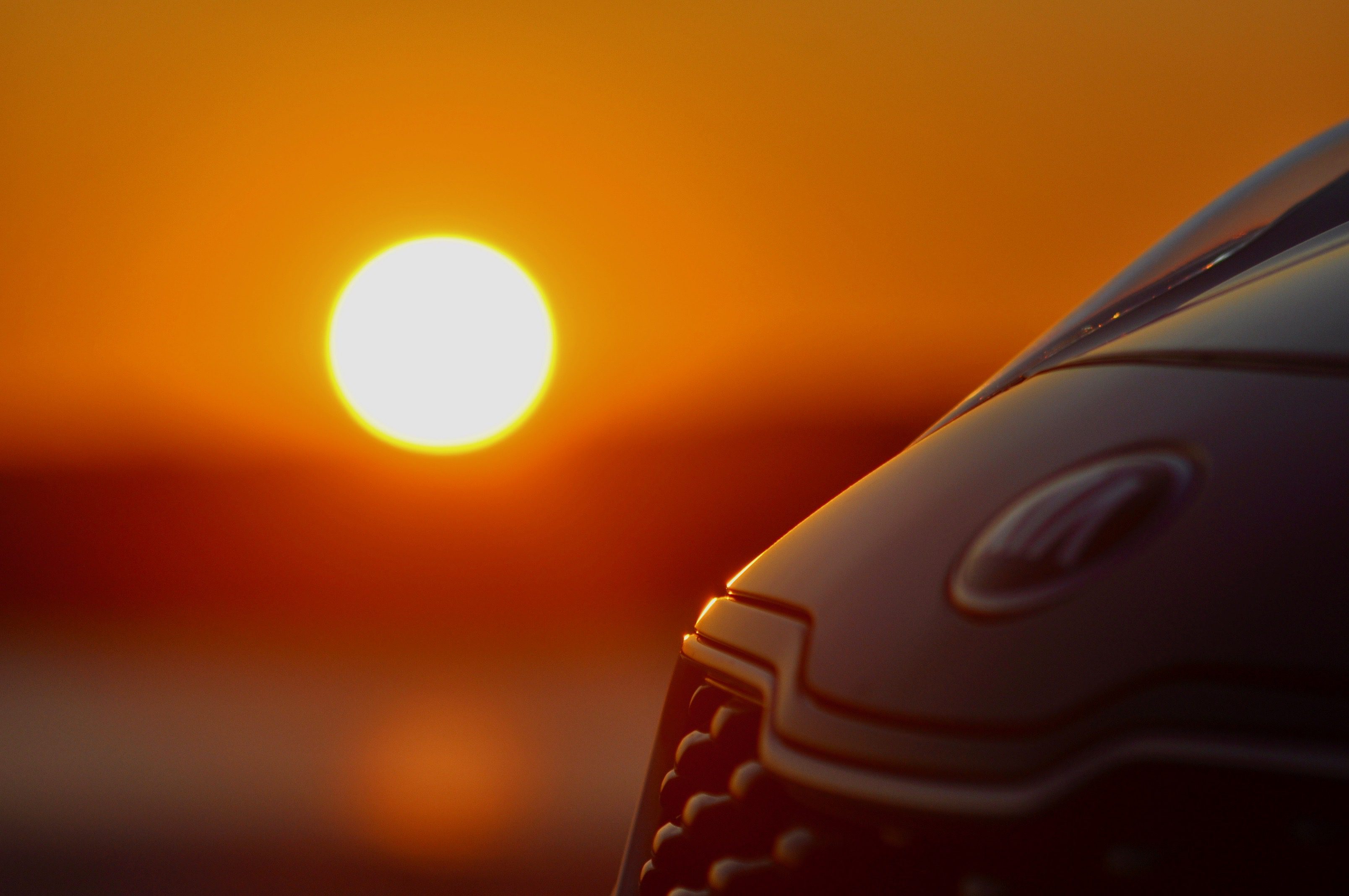 Close-up of a car's front grille with a vibrant sunset in the background.