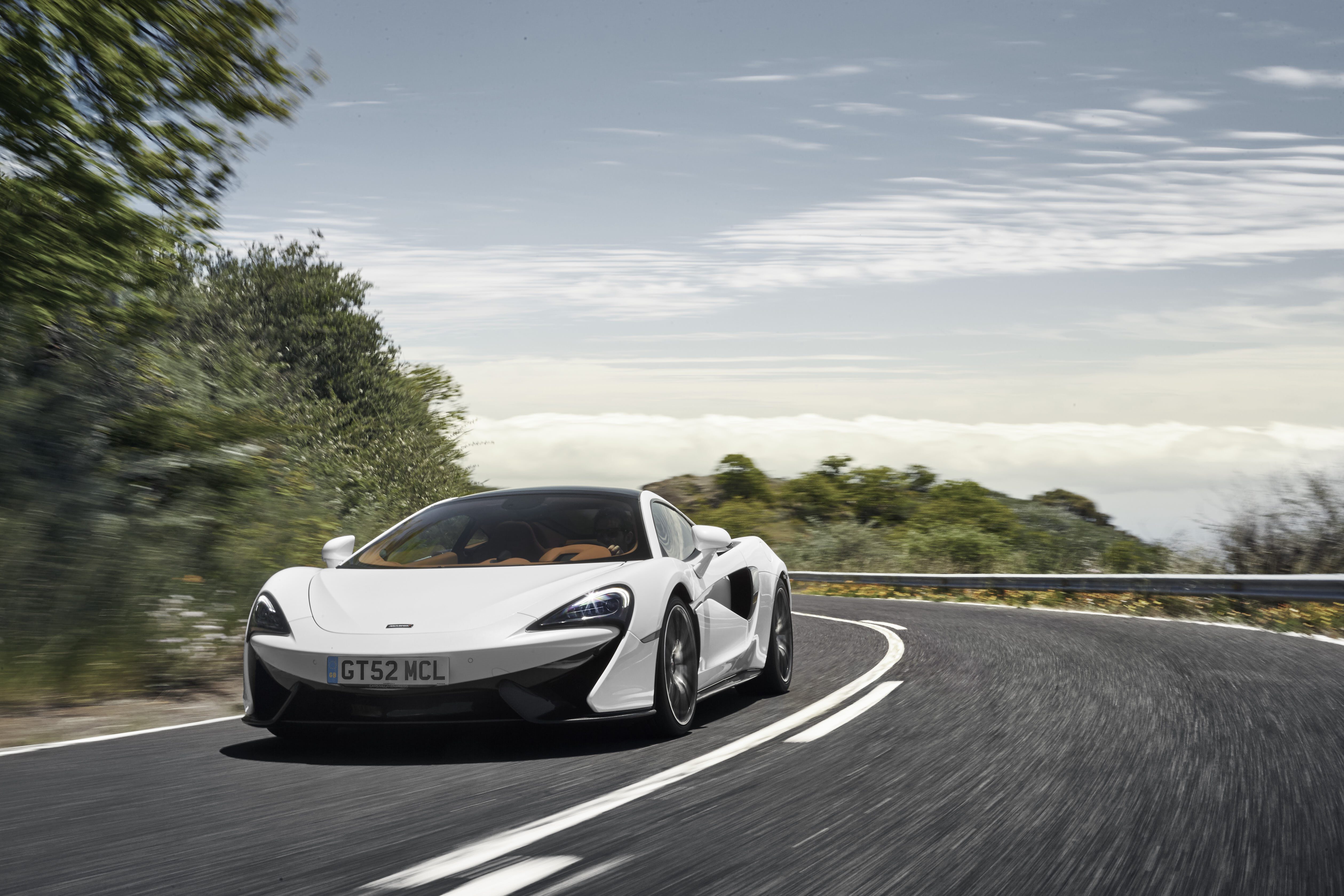 White sports car driving on a winding road surrounded by greenery.
