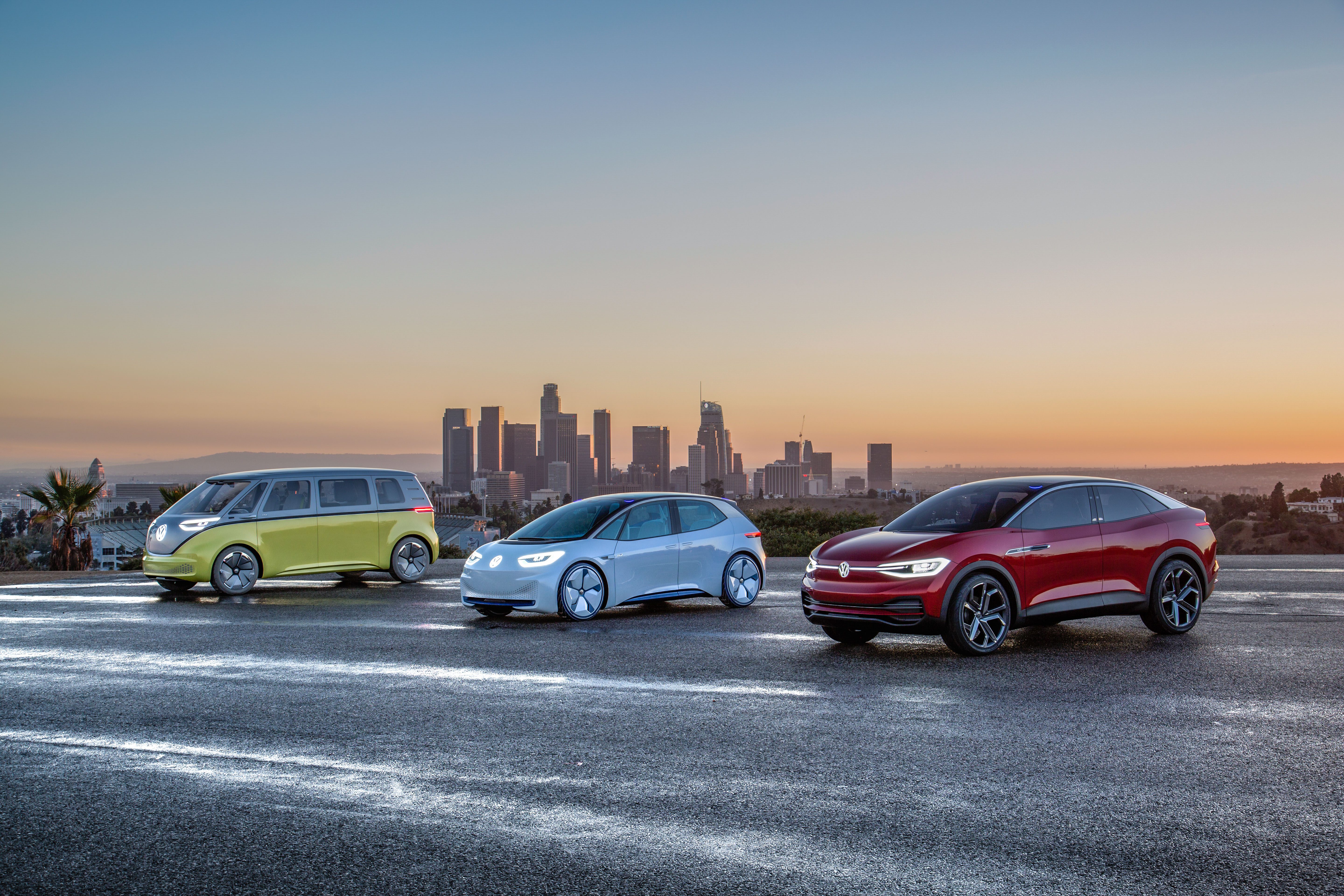 Three modern cars parked with a city skyline at sunset.