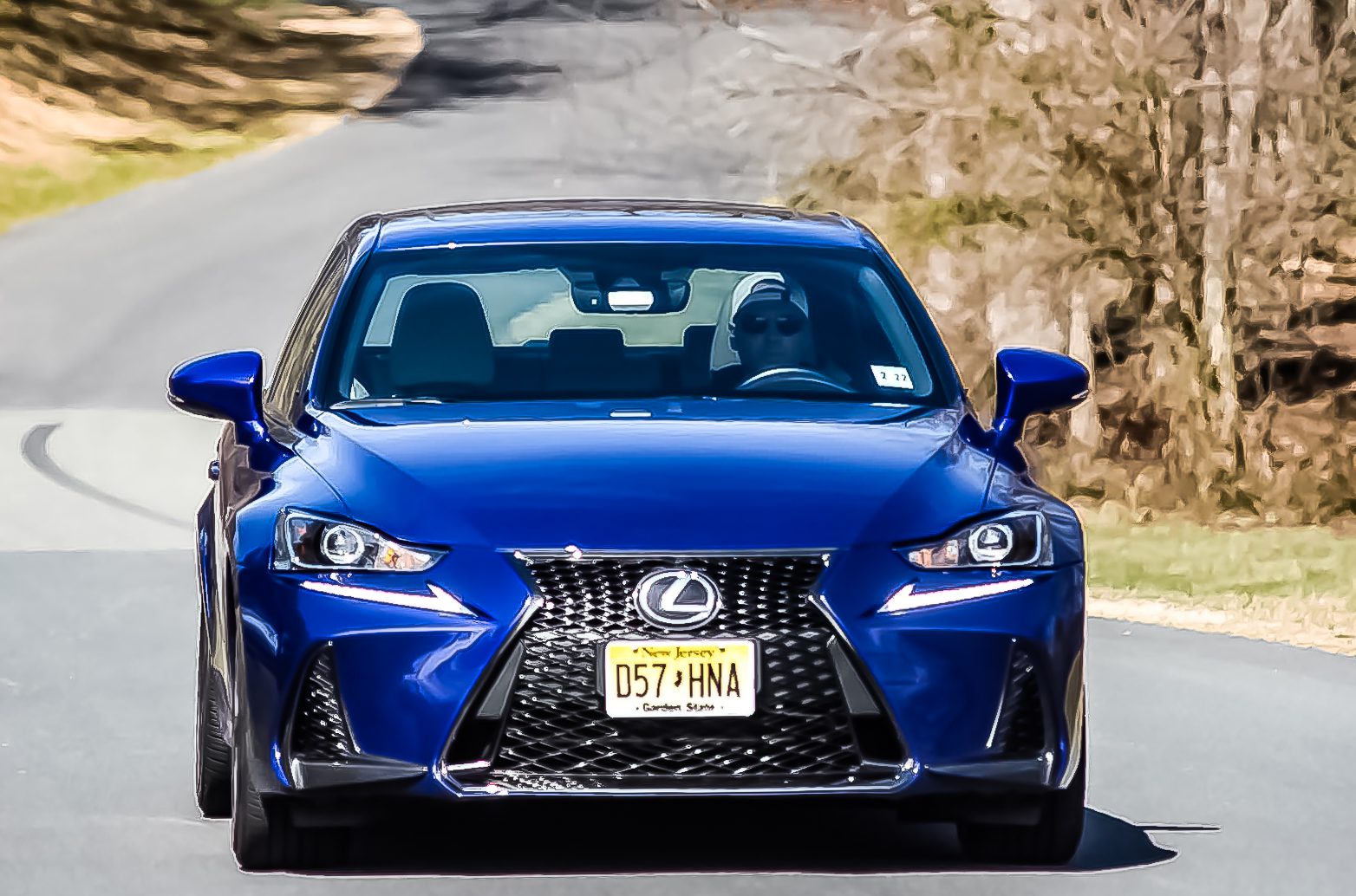 Blue Lexus car parked on a road with trees in the background.