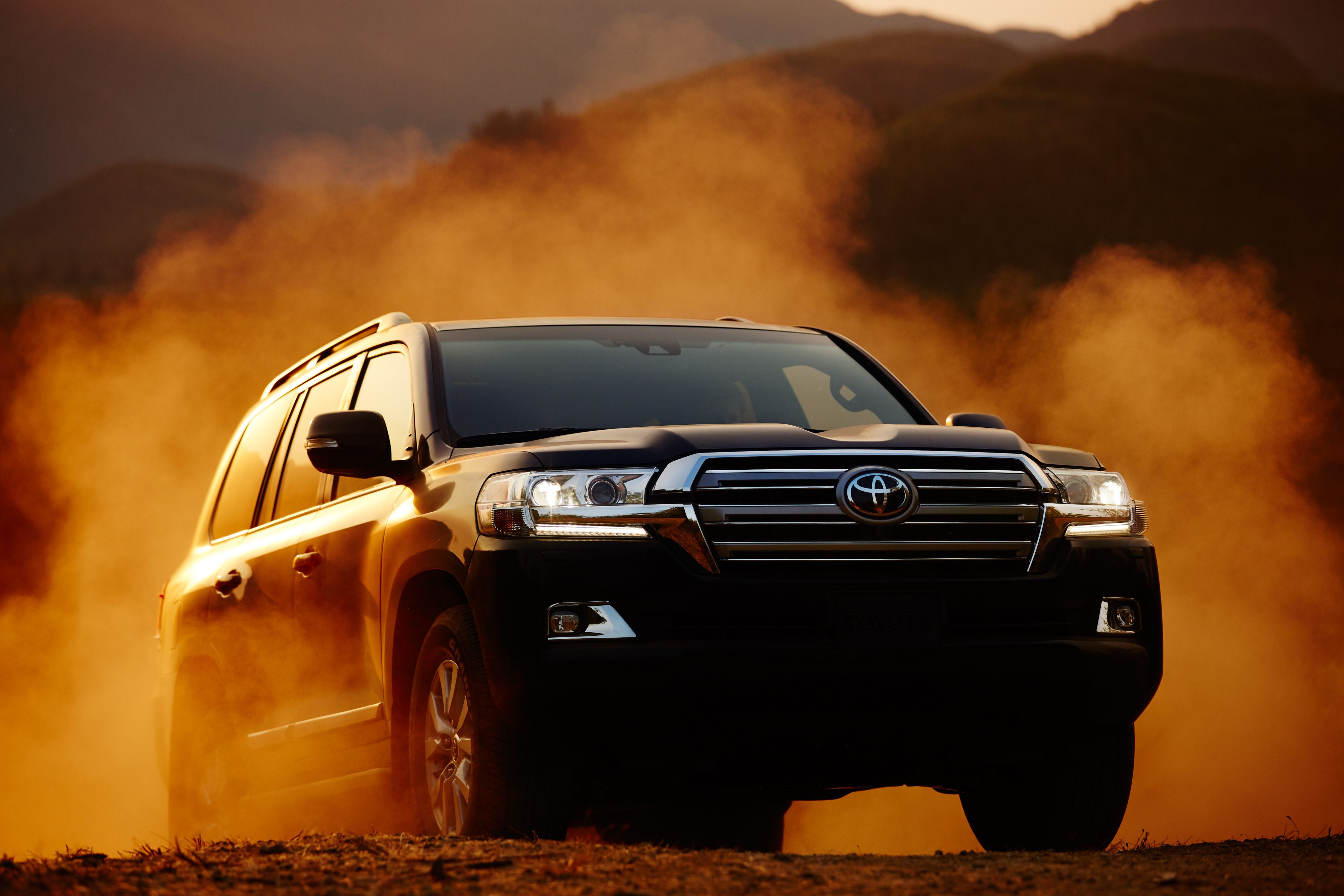 A black SUV driving through dusty terrain at sunset.