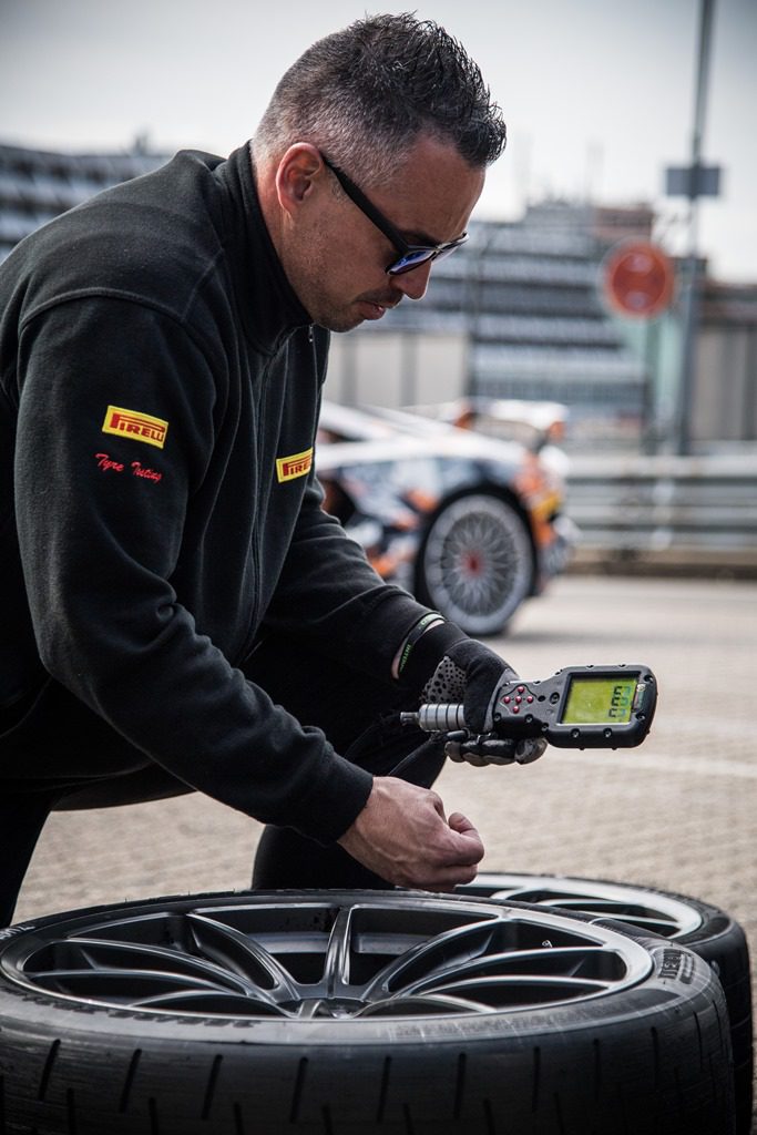 A man inspects a tire with a handheld device at a racetrack.