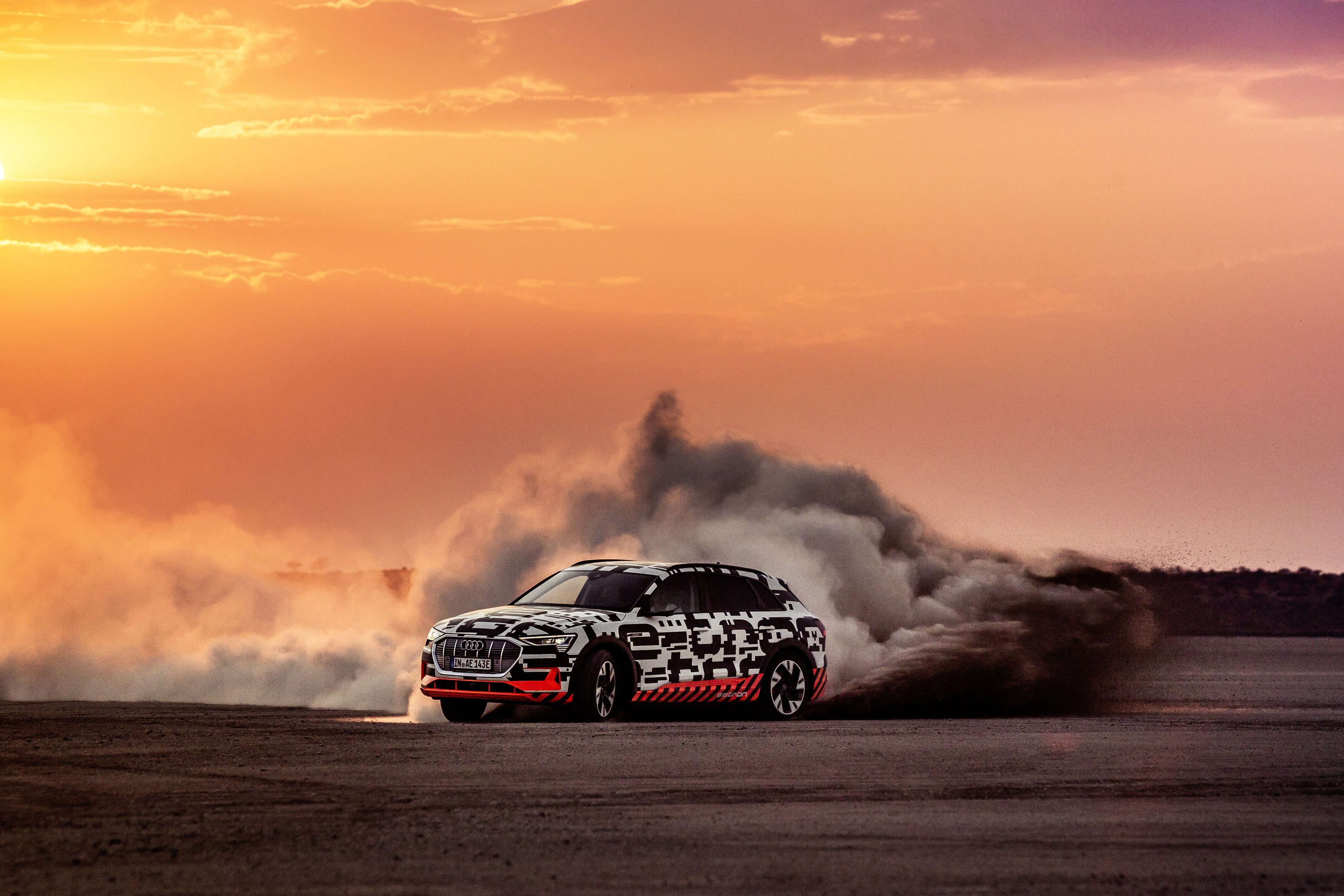 A red rally car kicking up dust during a sunset drift.