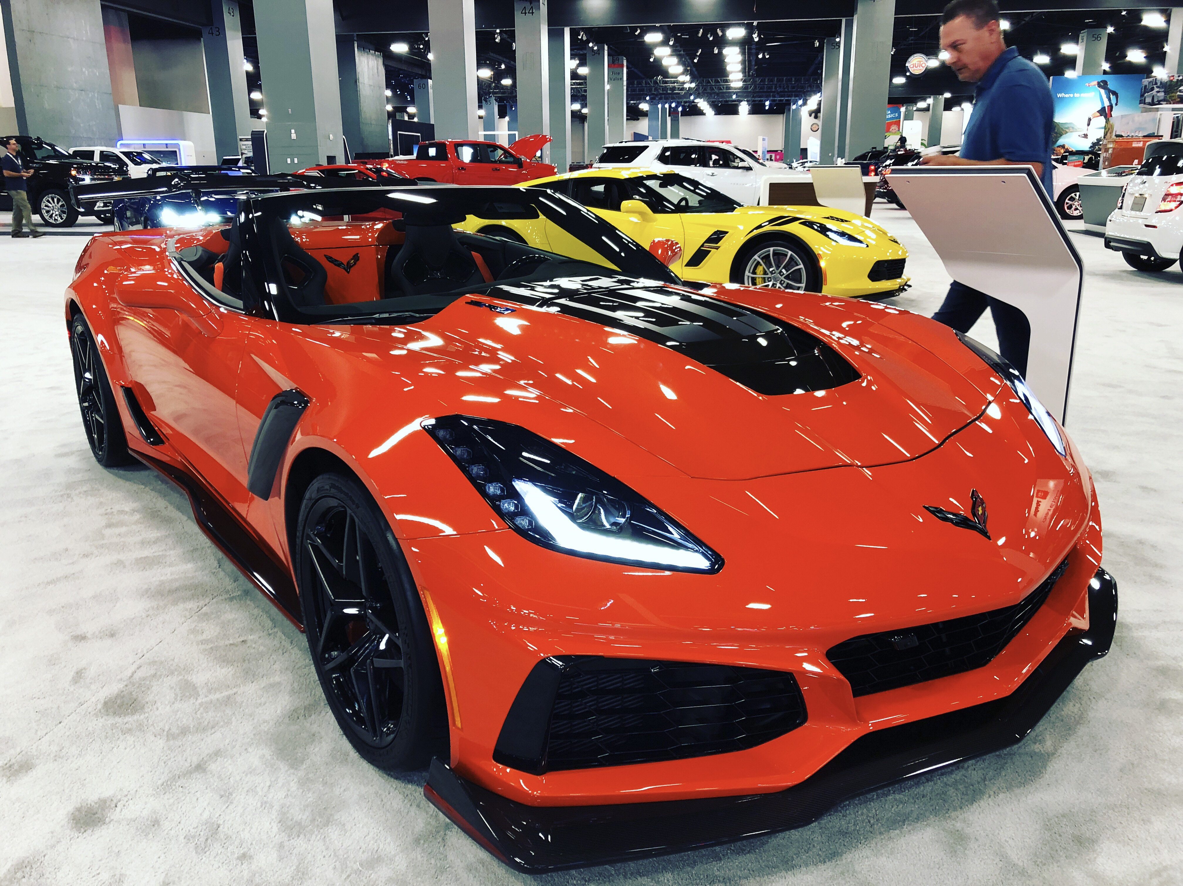 Bright orange sports car with black accents at an indoor auto show.