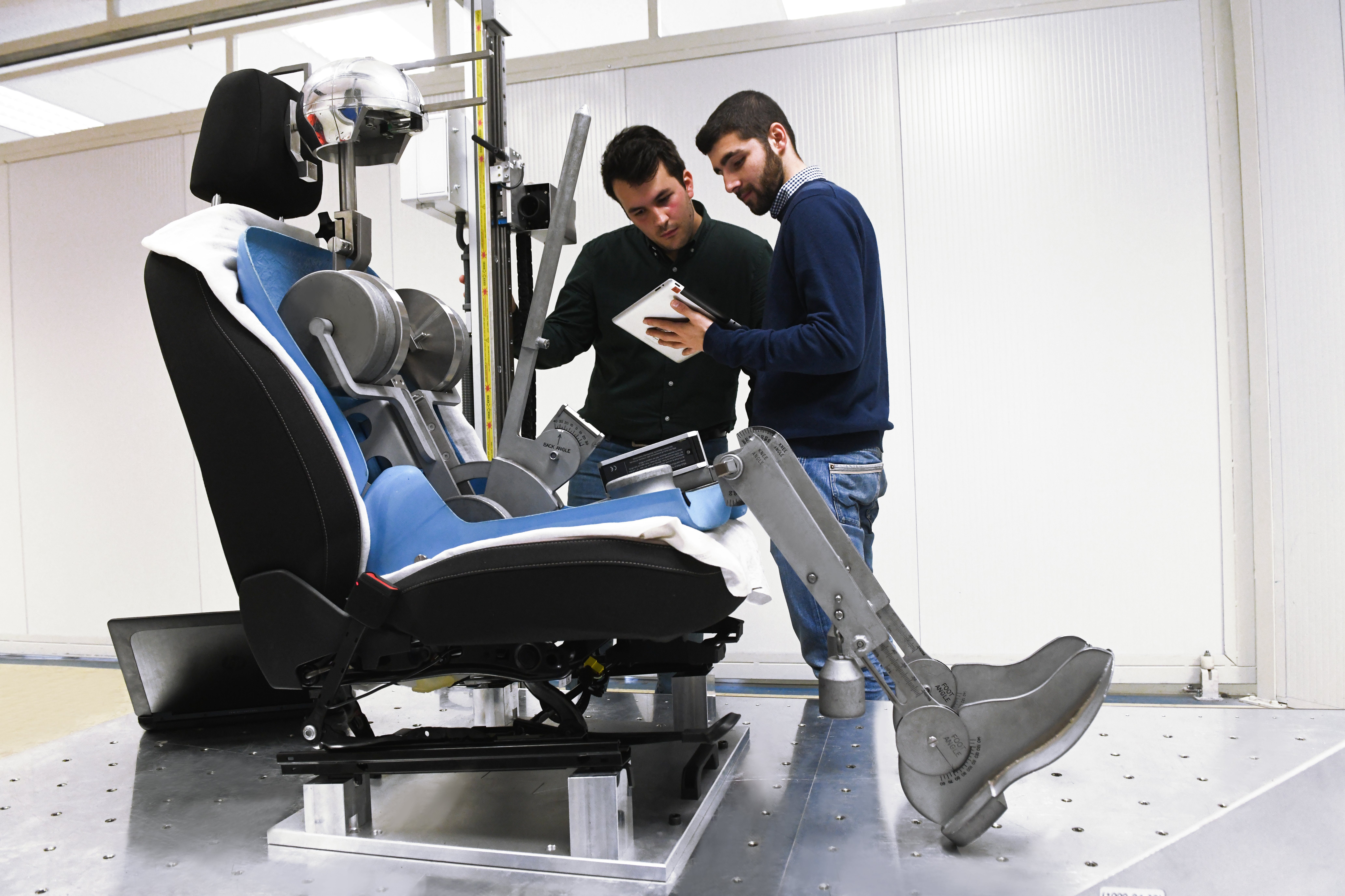 Two men inspecting a car seat and its mechanical components in a lab.
