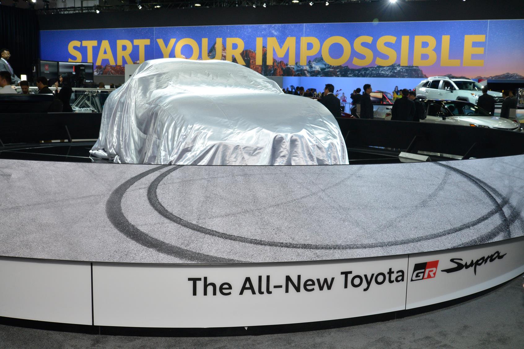 A covered Toyota car on a display platform with tire marks around it.