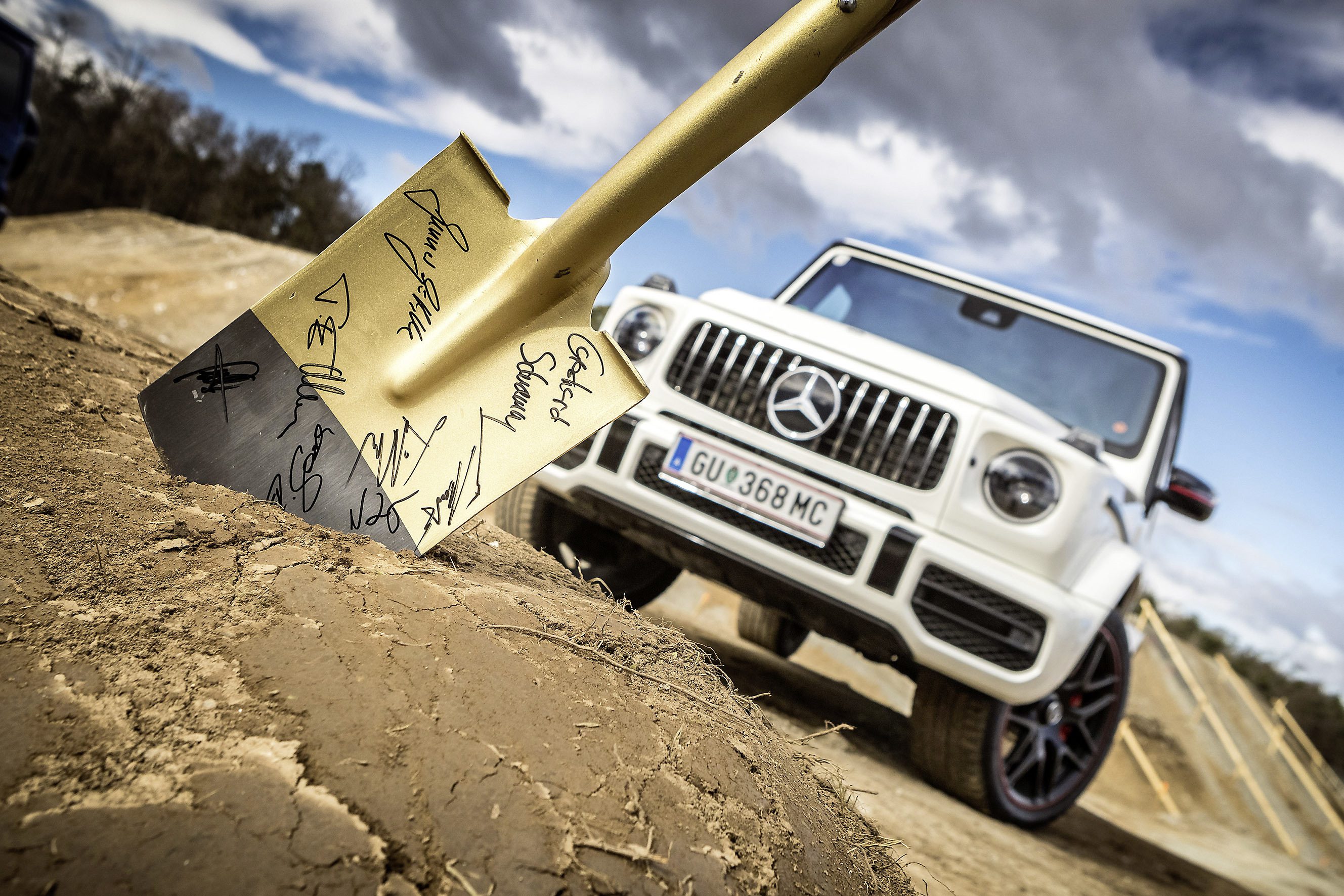 A white Mercedes-Benz SUV parked on dirt with a shovel in the foreground.