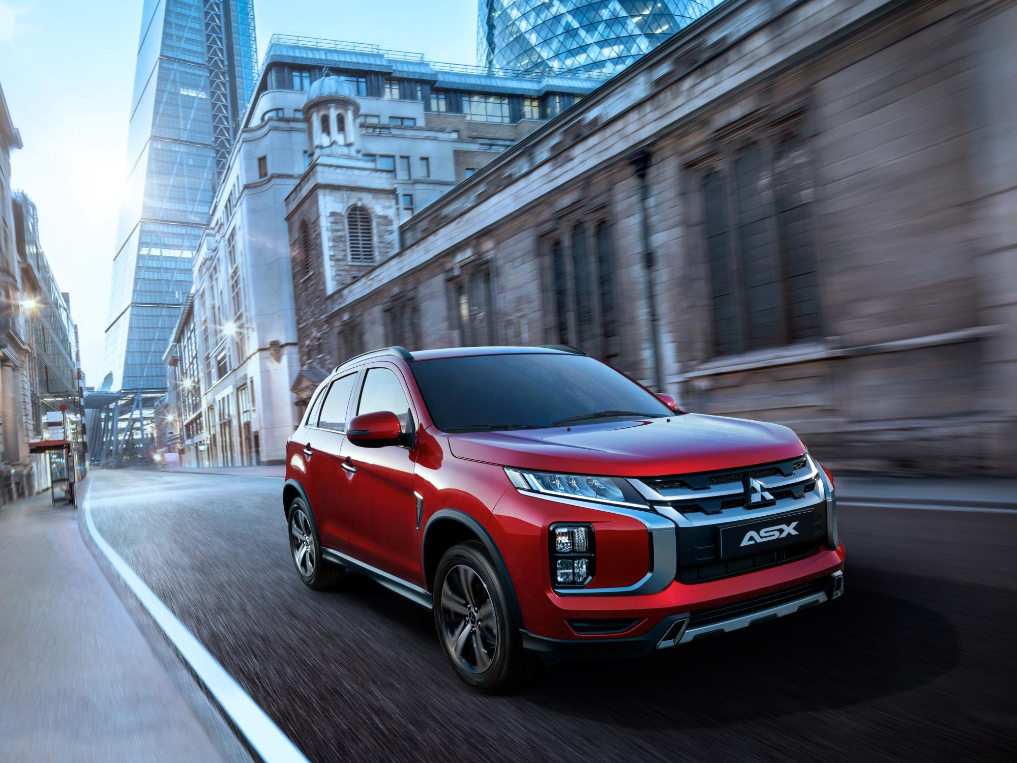 Red SUV driving through a city street with modern and historic buildings.