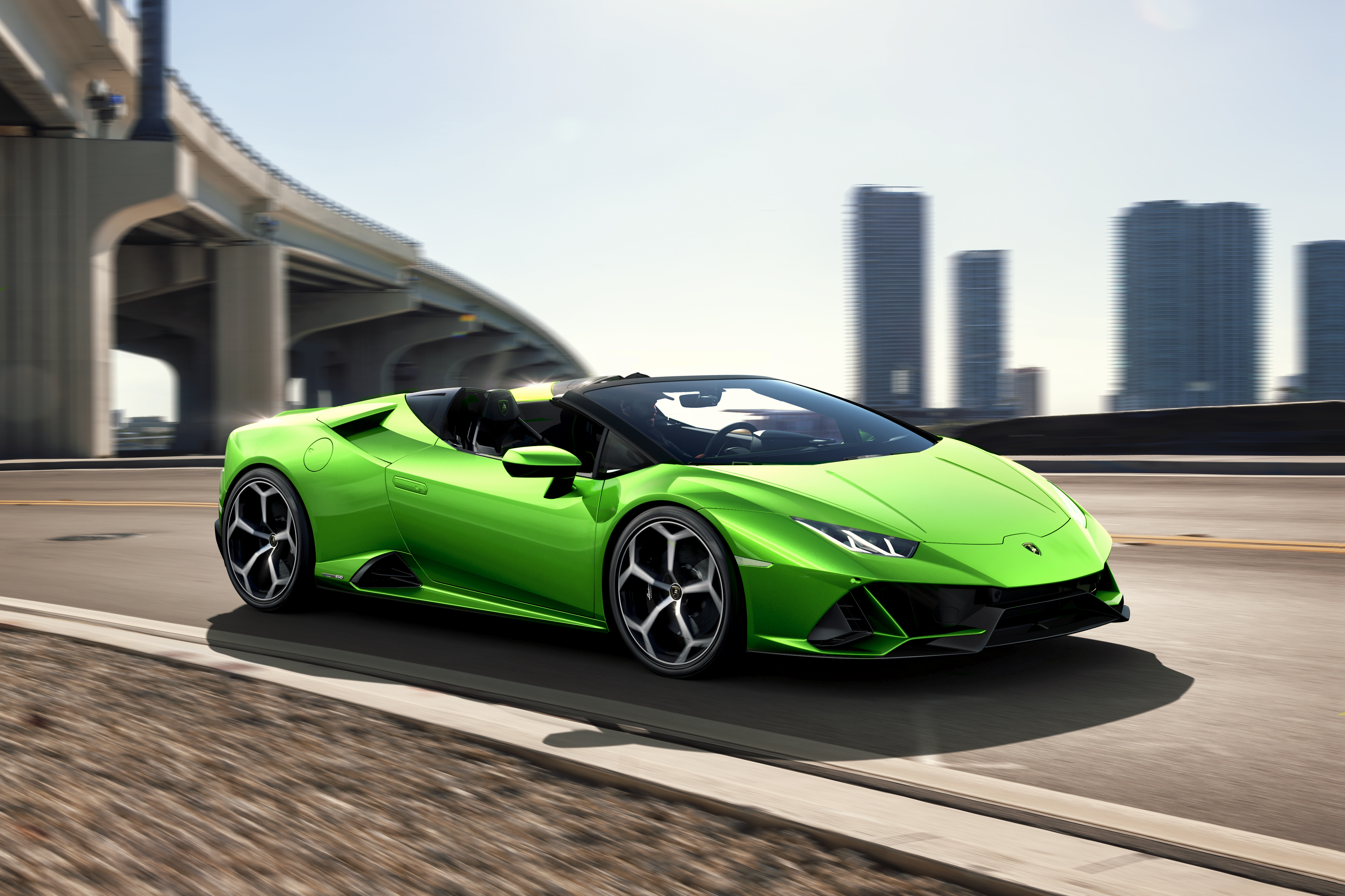 A vibrant green Lamborghini convertible parked near a city bridge.