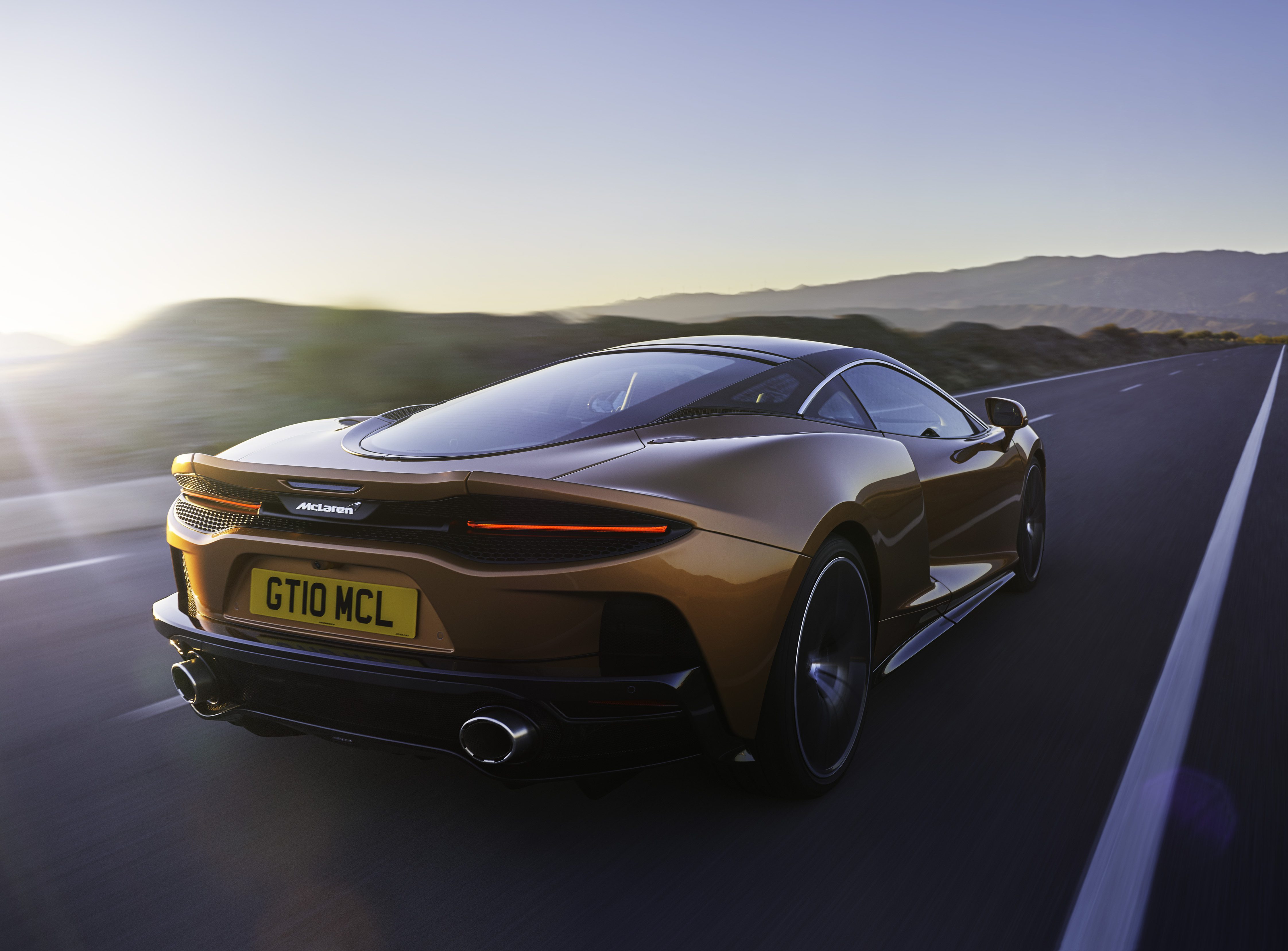 Sleek McLaren sports car driving on an open road at sunset.