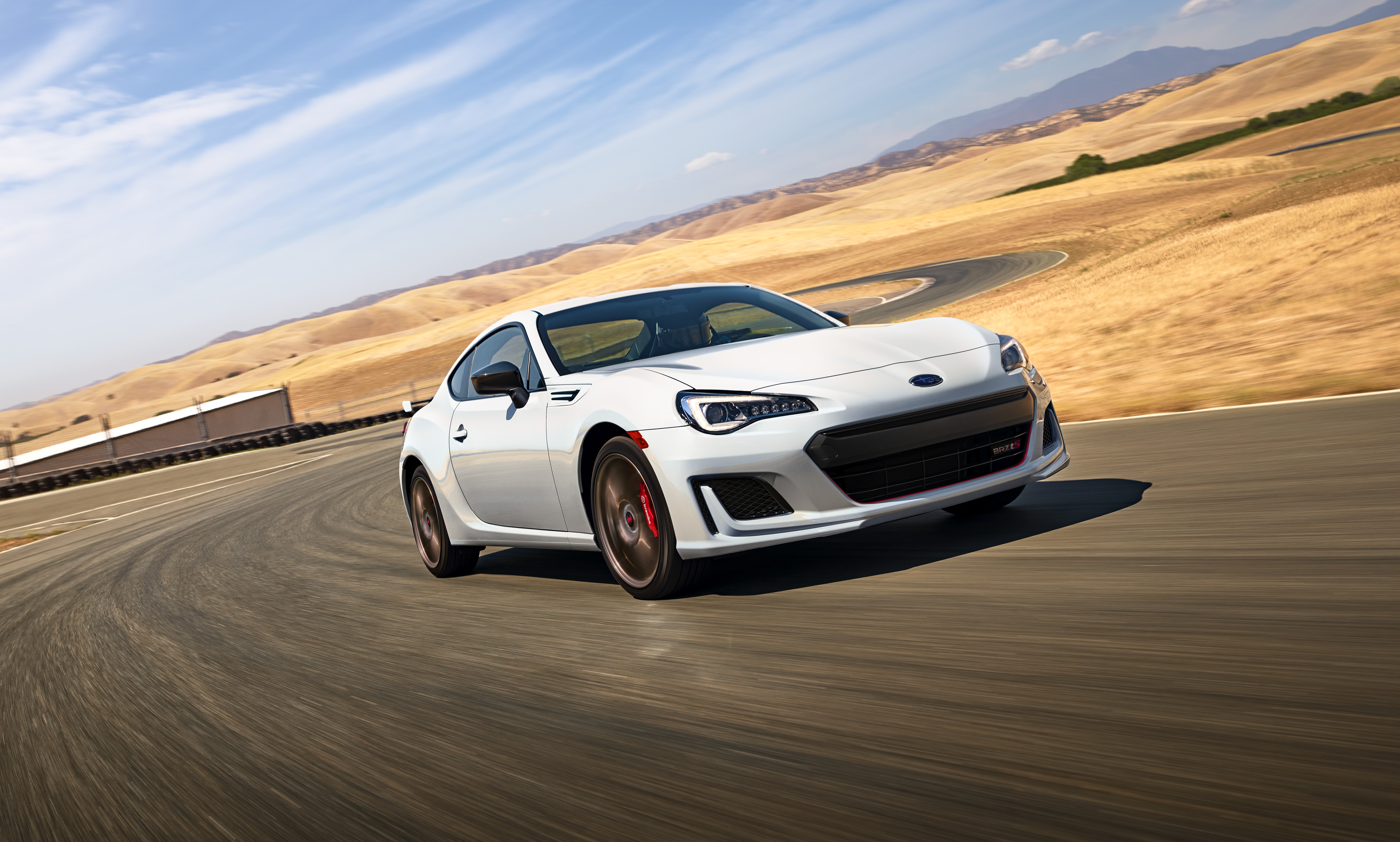 White sports car speeding on a desert road under a clear sky.