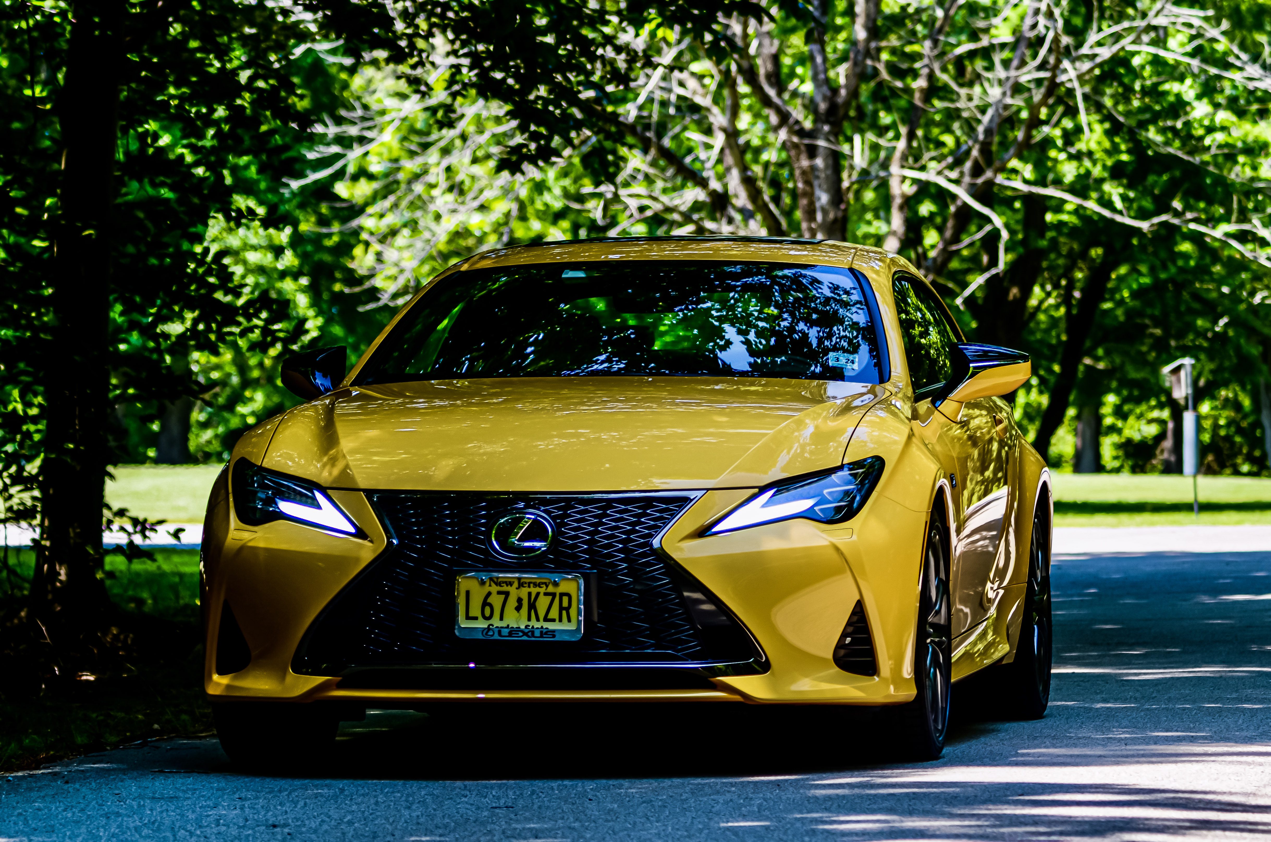 Yellow Lexus sports car driving on a tree-lined road.