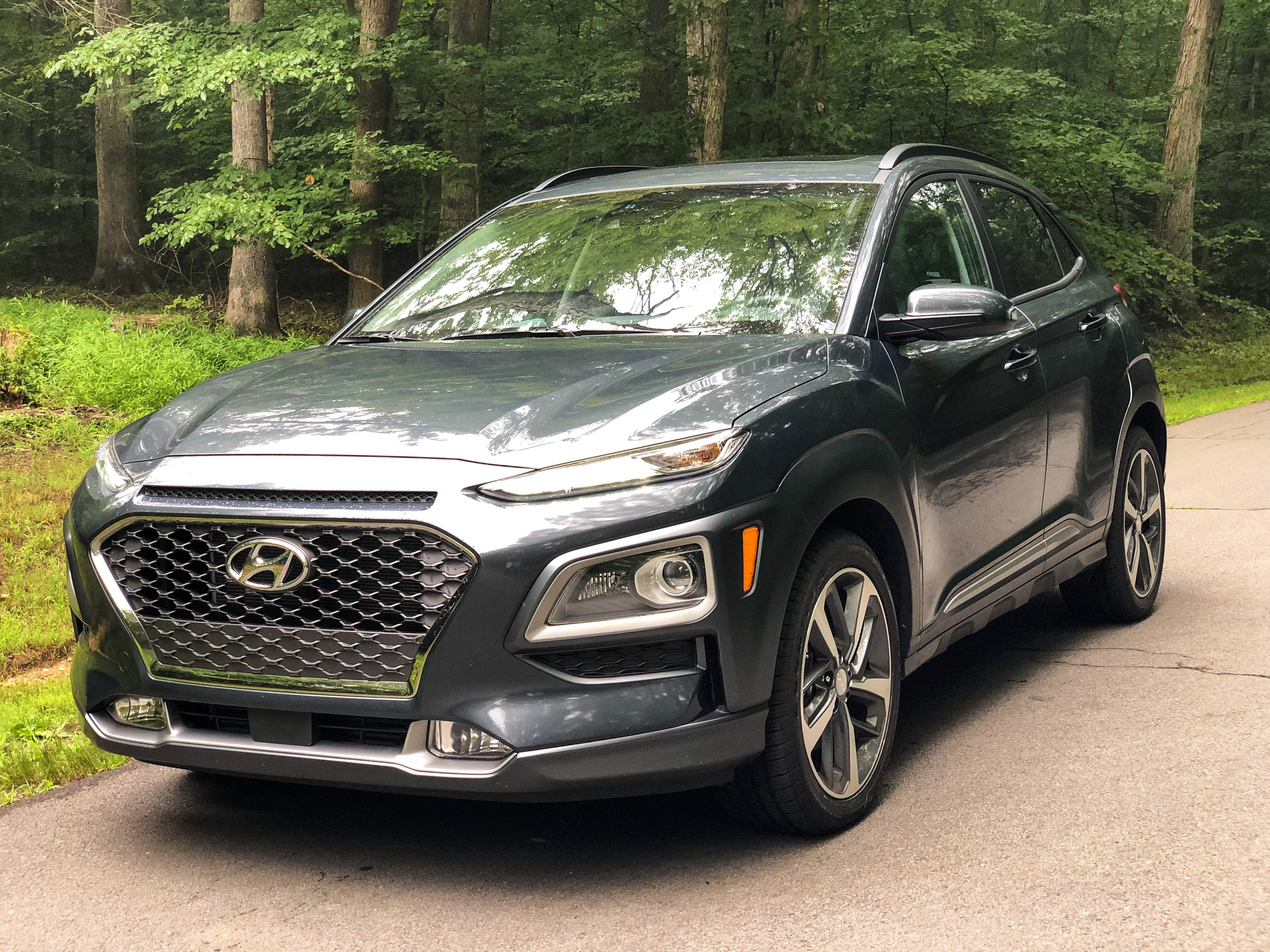 A sleek black Hyundai Kona parked on a forest road.