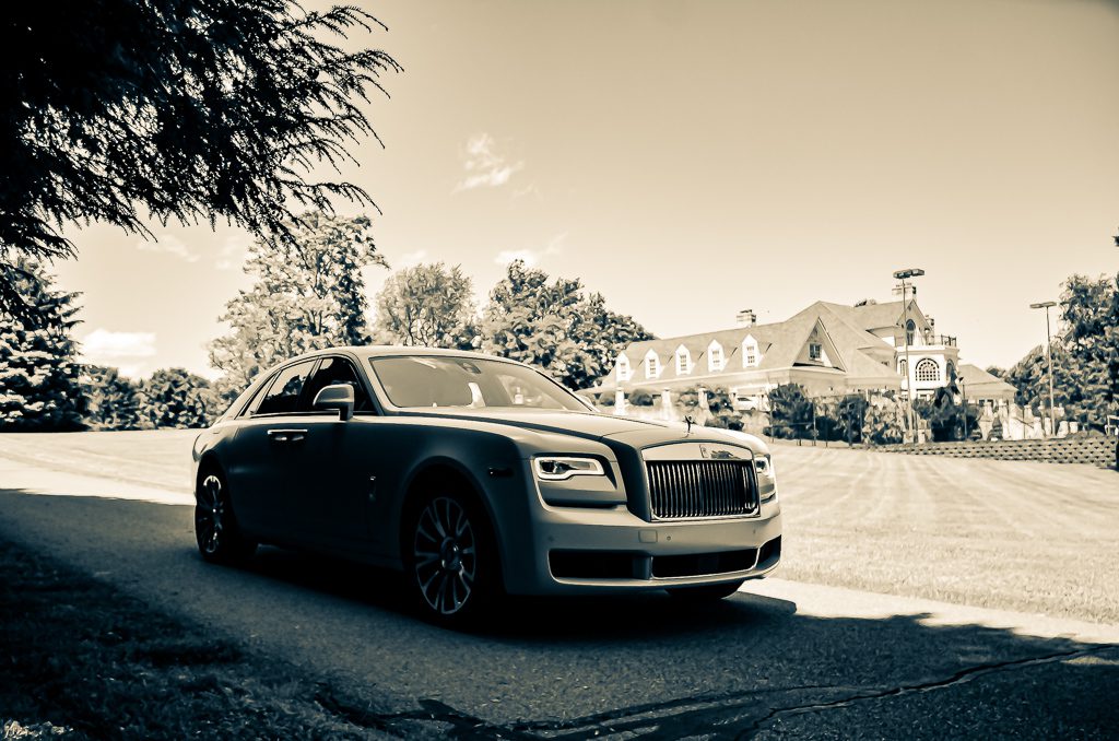 A sleek Rolls-Royce parked on a suburban street in sepia tone.