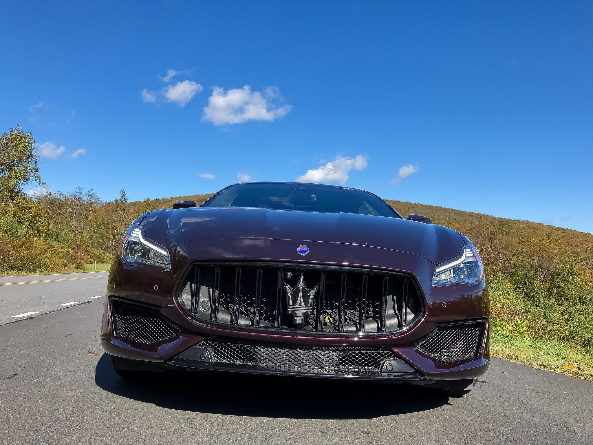 Front view of a sleek black Maserati on a road under blue sky.