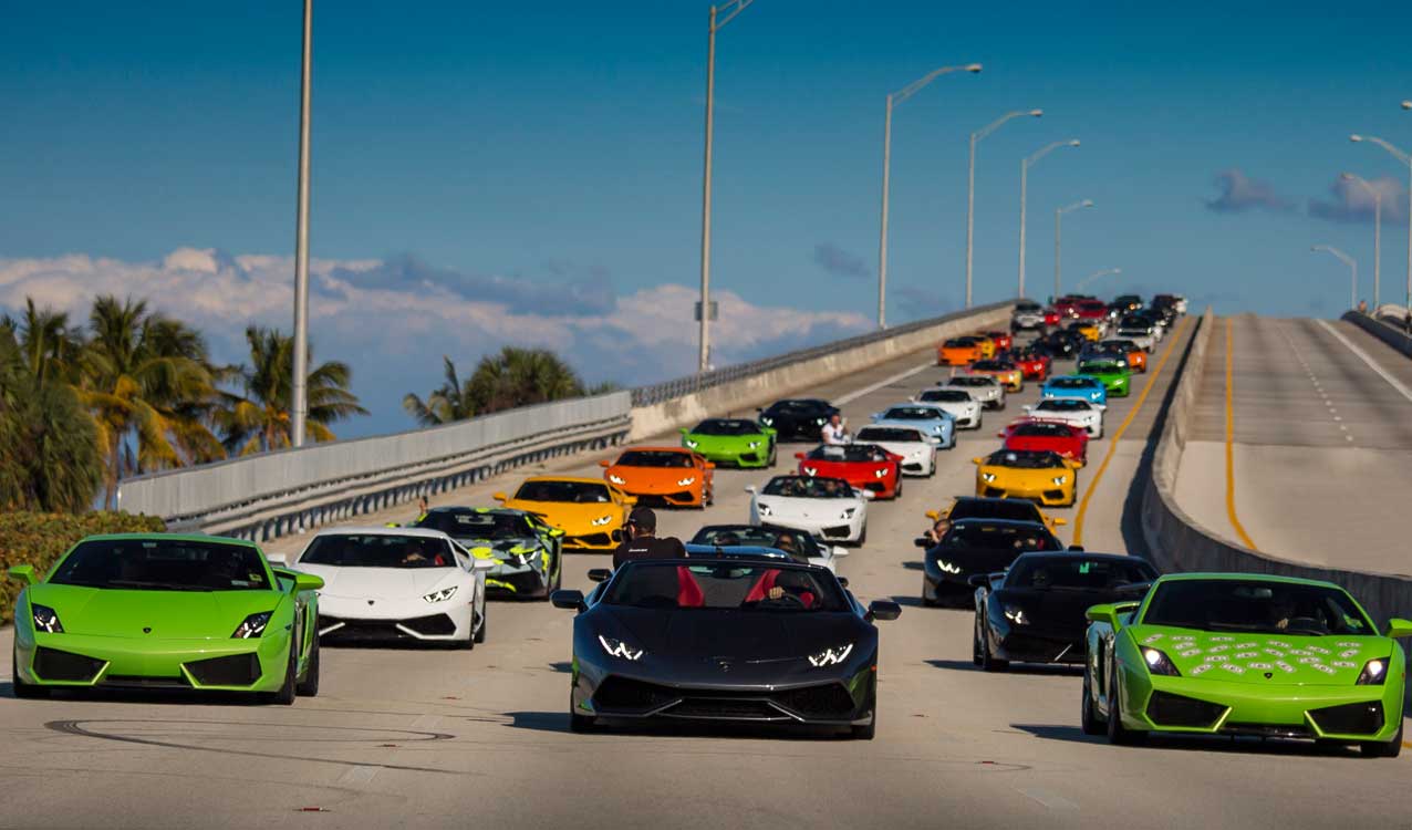 A convoy of exotic sports cars driving on a sunny highway.