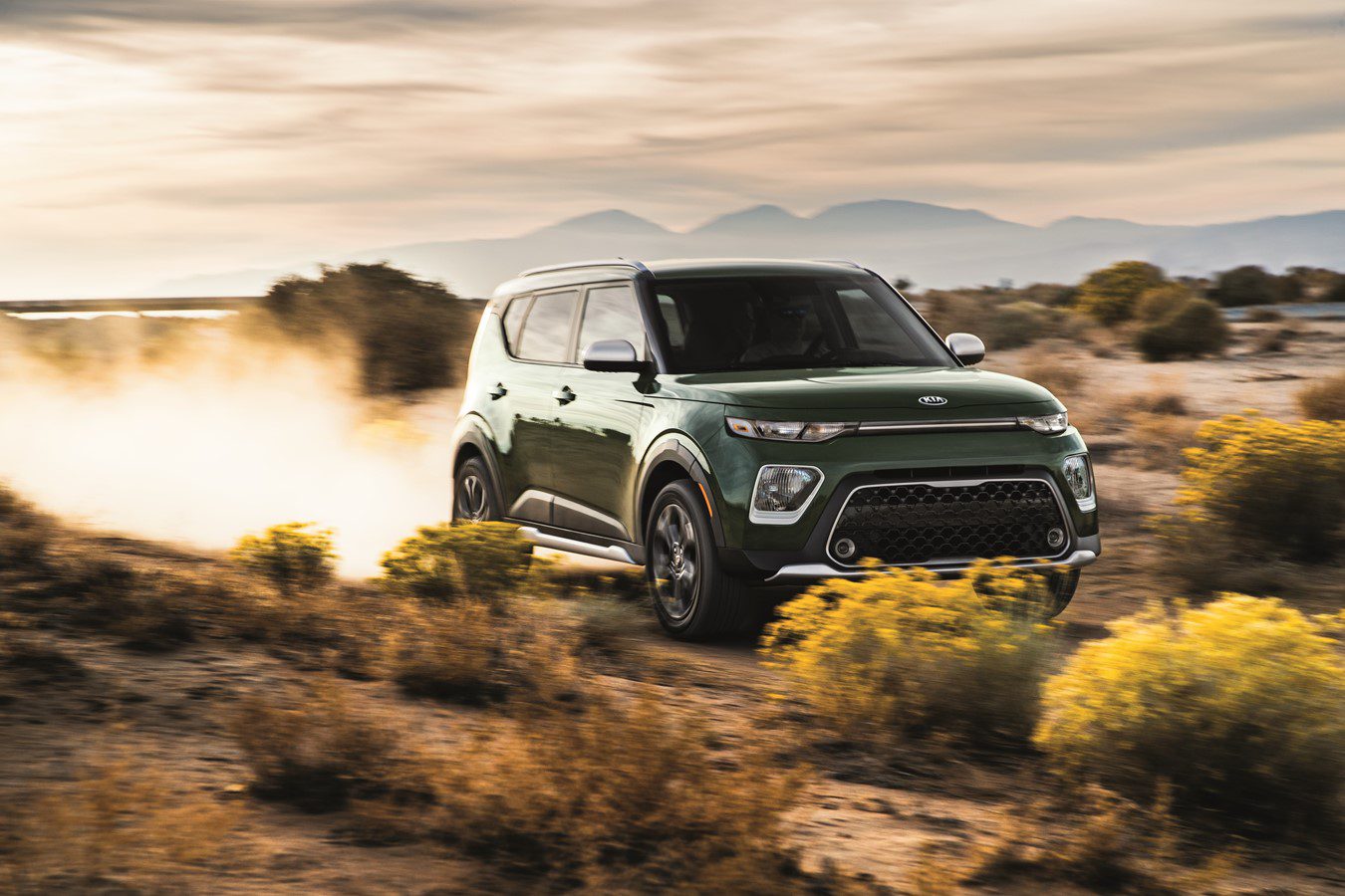 A green SUV driving through a desert landscape at sunset.